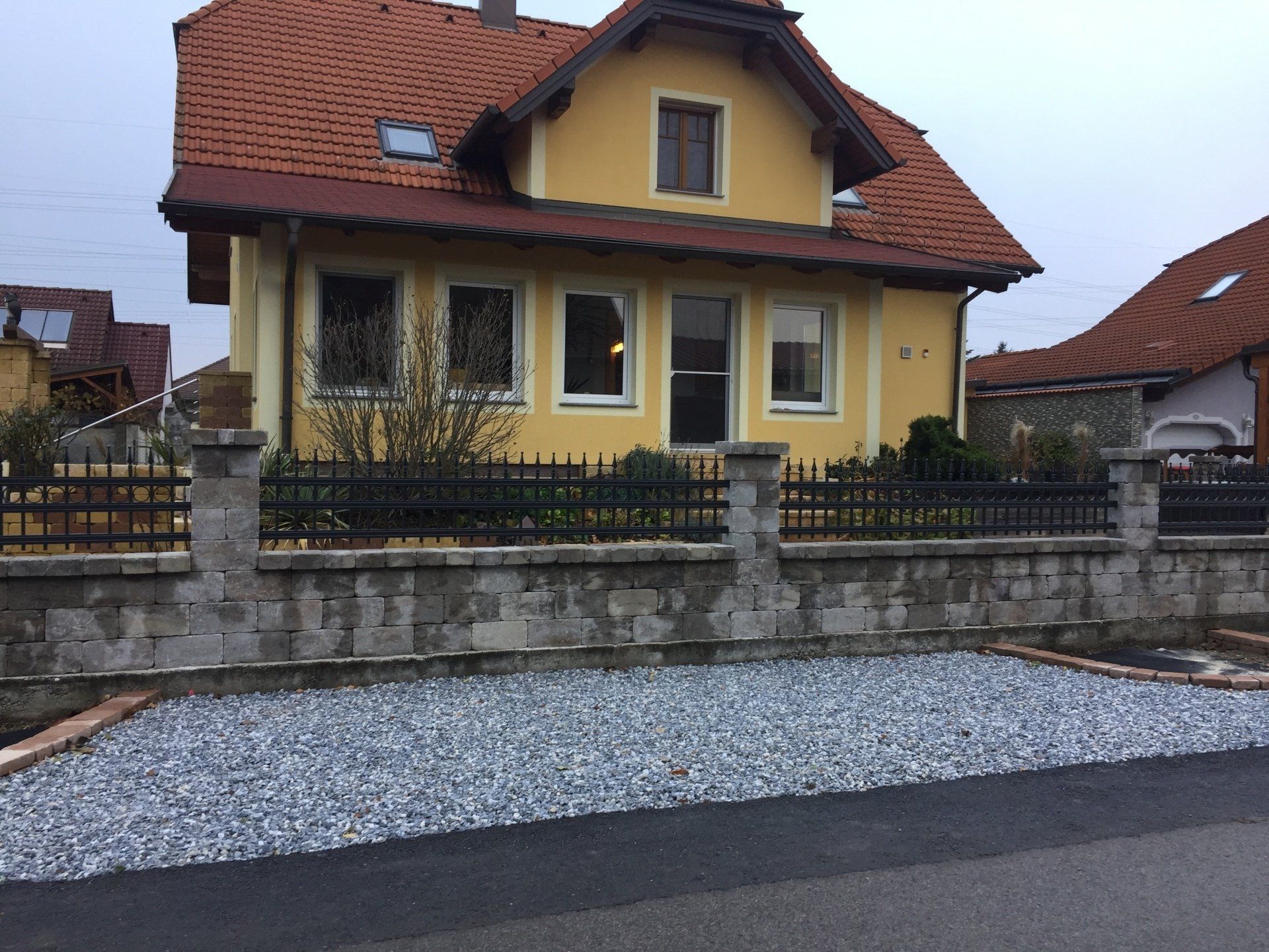 Ein gelbes Haus mit einem Zaun und Kies davor