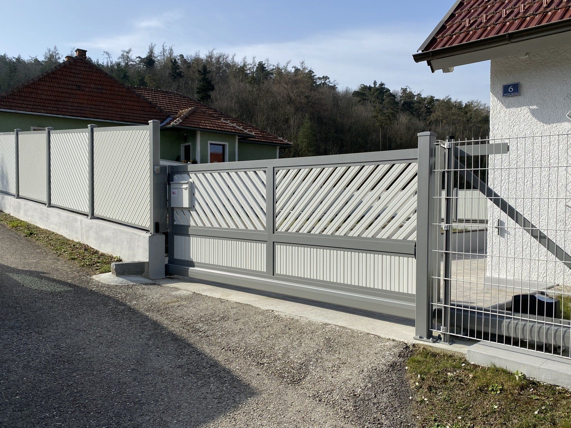 Ein weißer Zaun mit einem Schiebetor vor einem Haus.