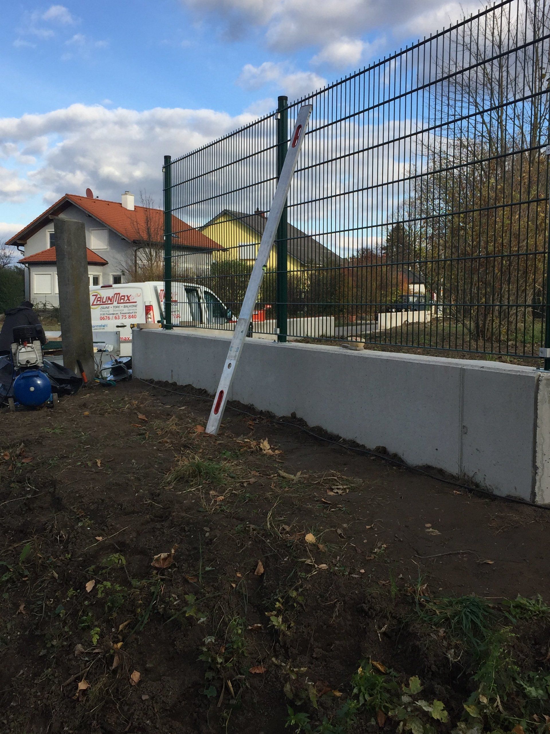 Neben einer Betonmauer wird ein Zaun gebaut.