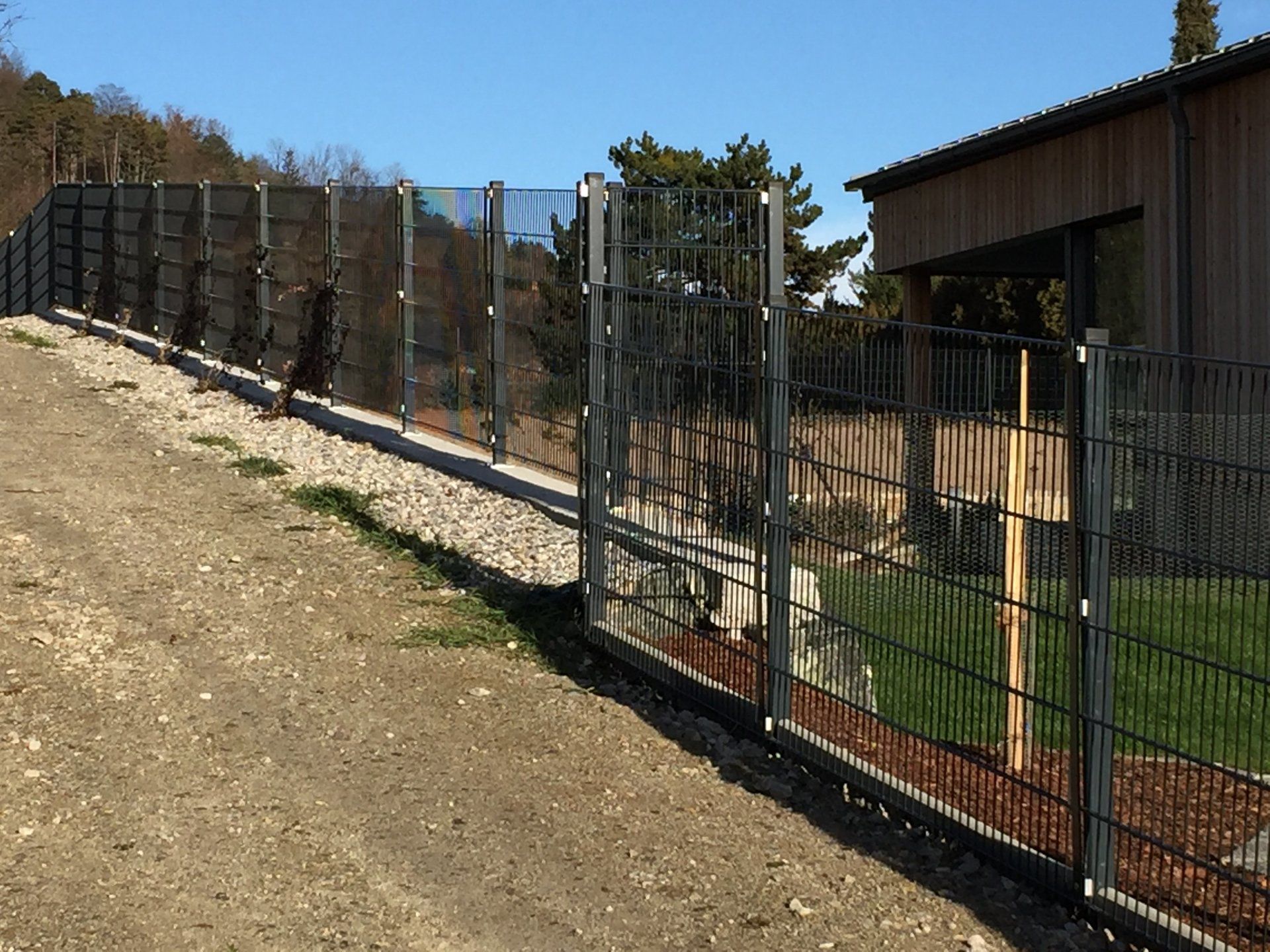 Ein Metallzaun umgibt eine Schotterstraße vor einem Haus.