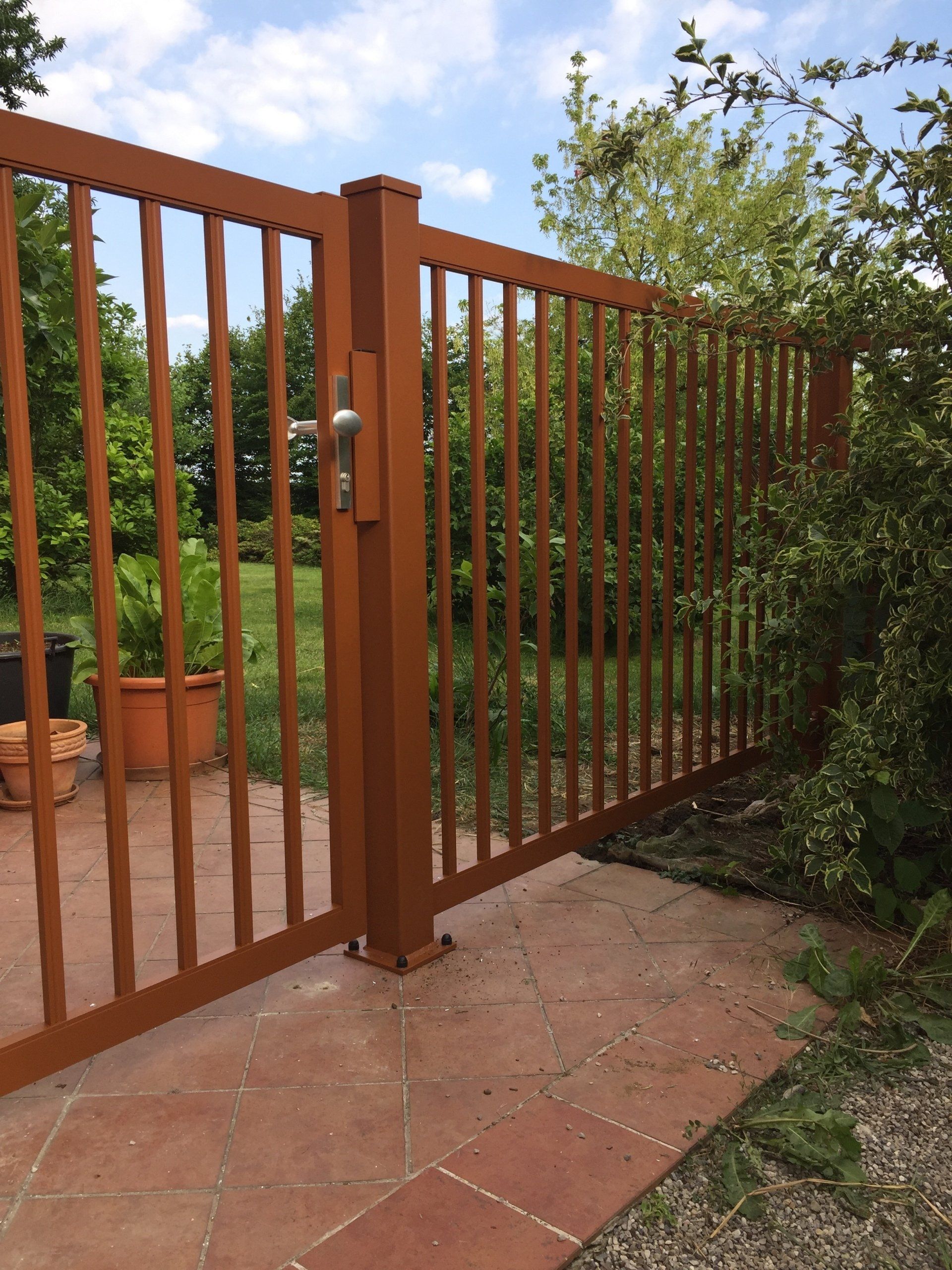 Ein Holztor führt zu einer Terrasse mit Topfpflanzen dahinter