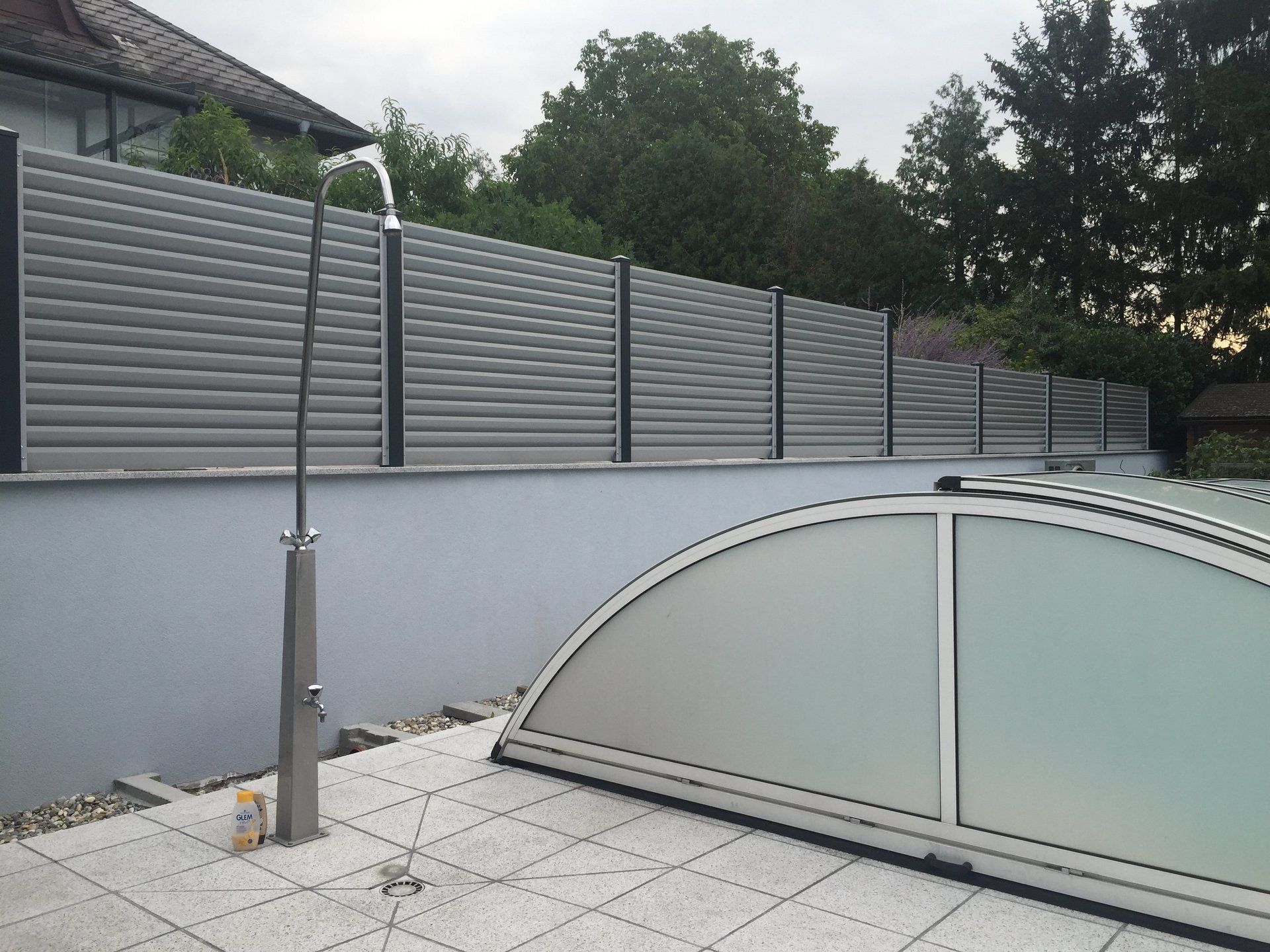 Ein Zaun umgibt einen Swimmingpool mit einer Dusche davor