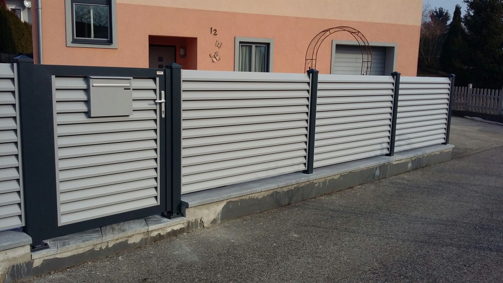 Ein weißer Zaun mit einem schwarzen Tor vor einem Haus