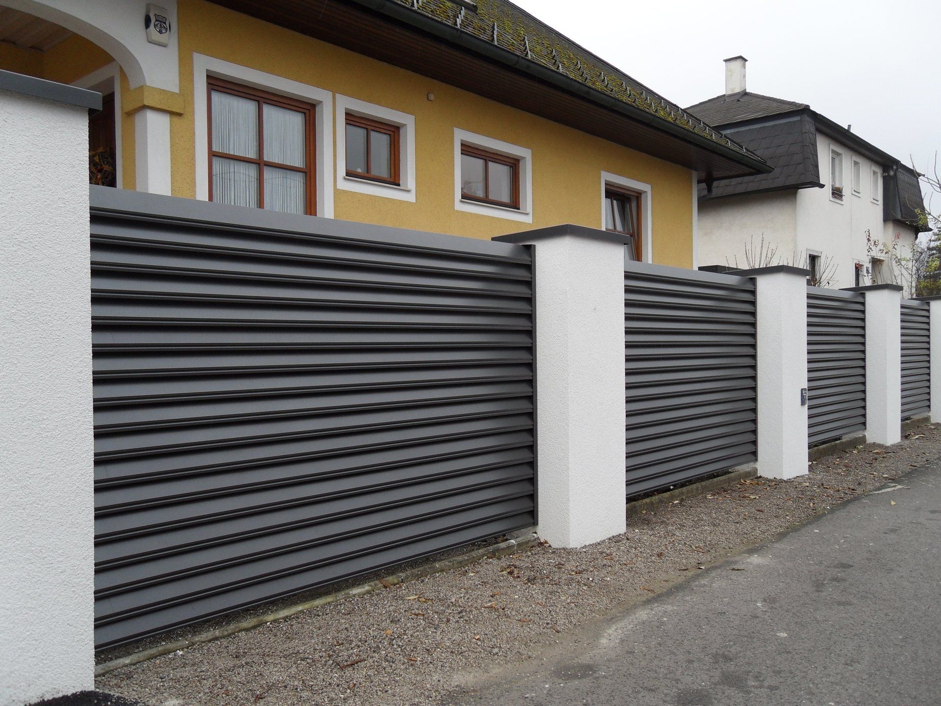 Ein gelbes Haus mit einem schwarzen Zaun davor