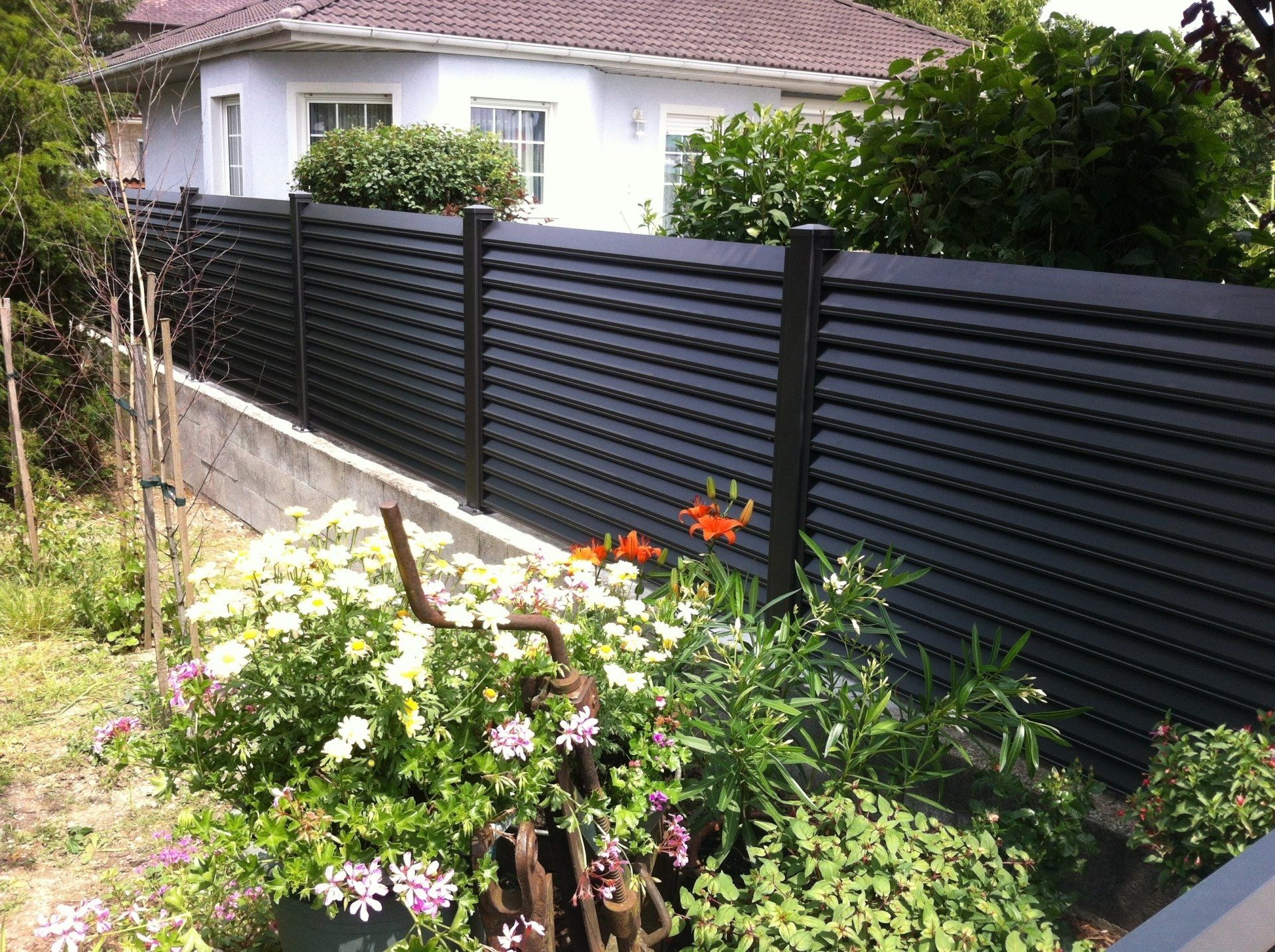Ein schwarzer Zaun umgibt einen Garten mit Blumen vor einem Haus