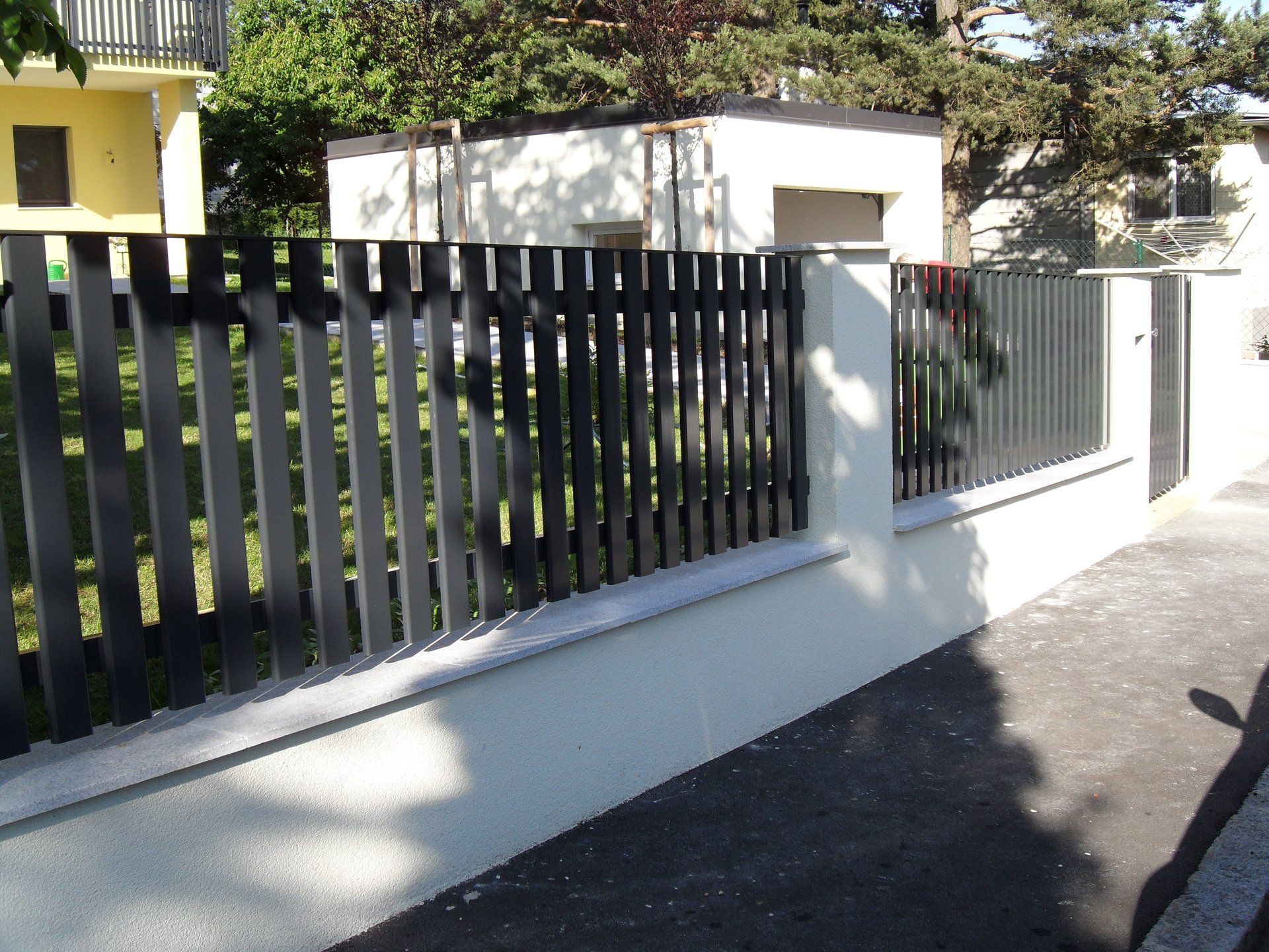 Eine weiße Wand mit einem schwarzen Zaun davor