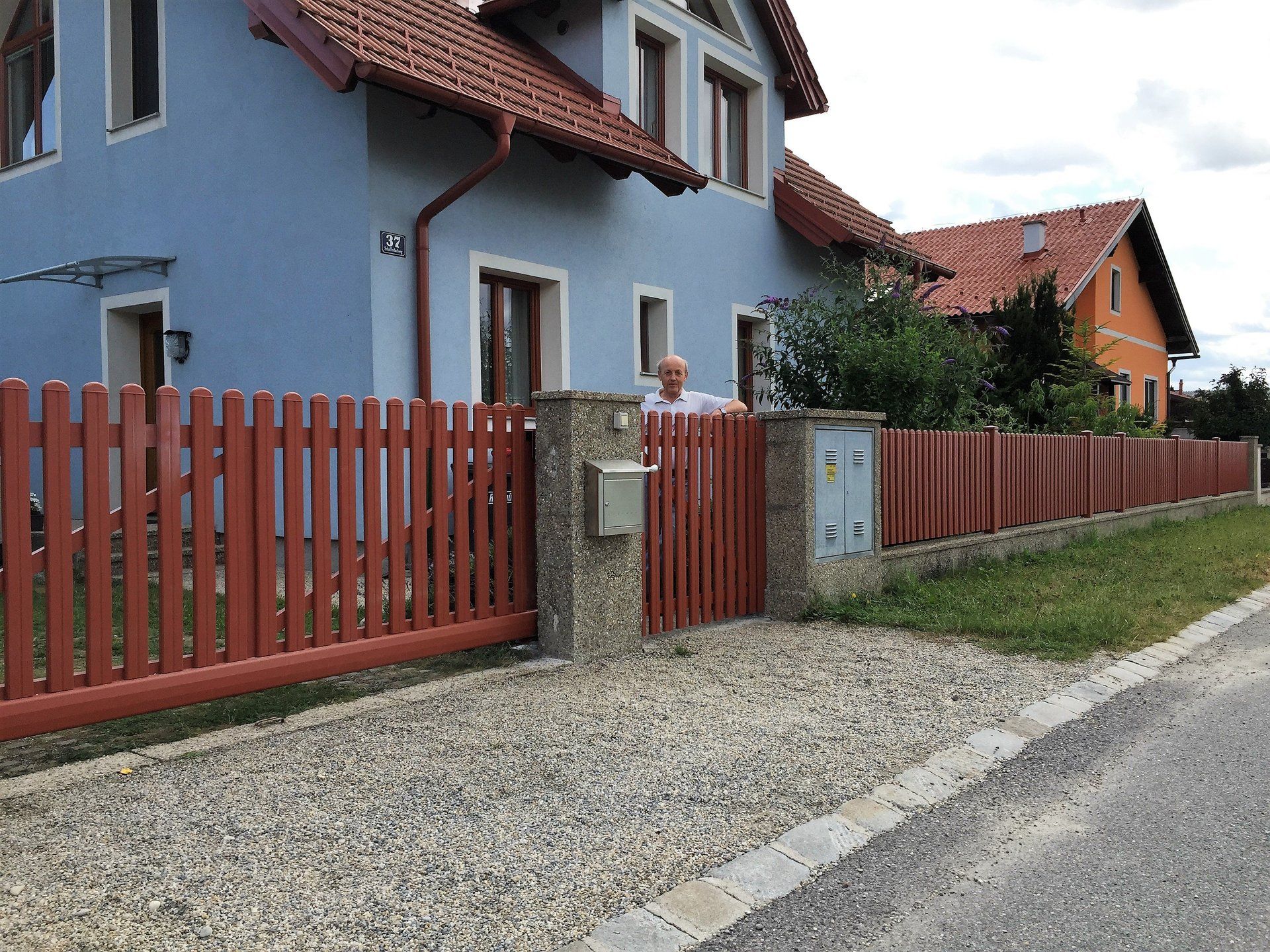 Ein Mann steht vor einem blauen Haus mit einem roten Zaun