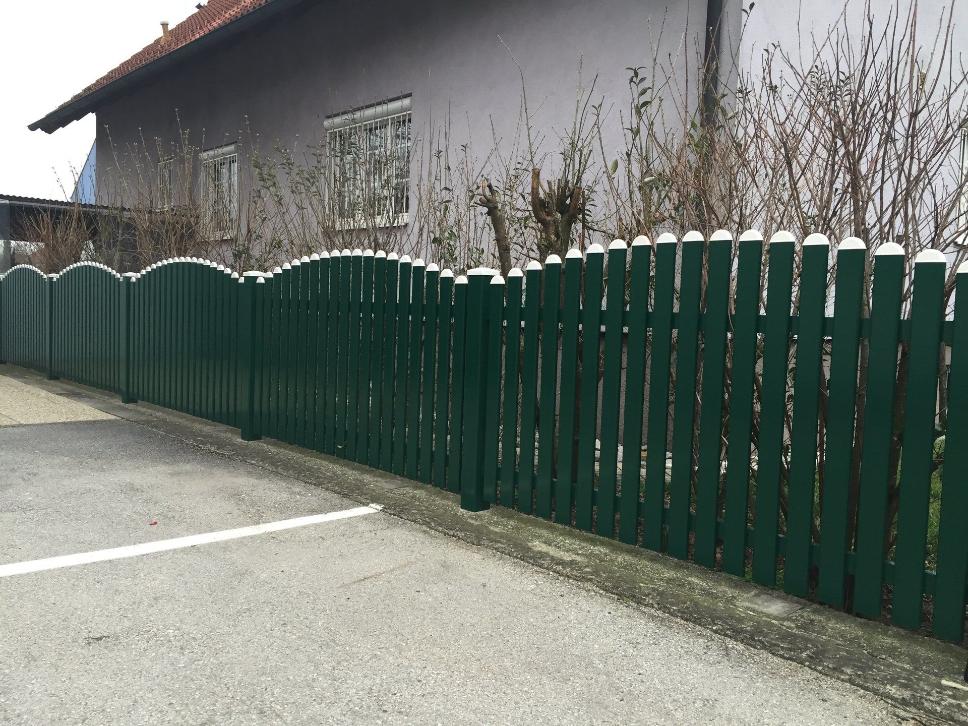 Vor einem Haus steht am Straßenrand ein grüner Holzzaun.