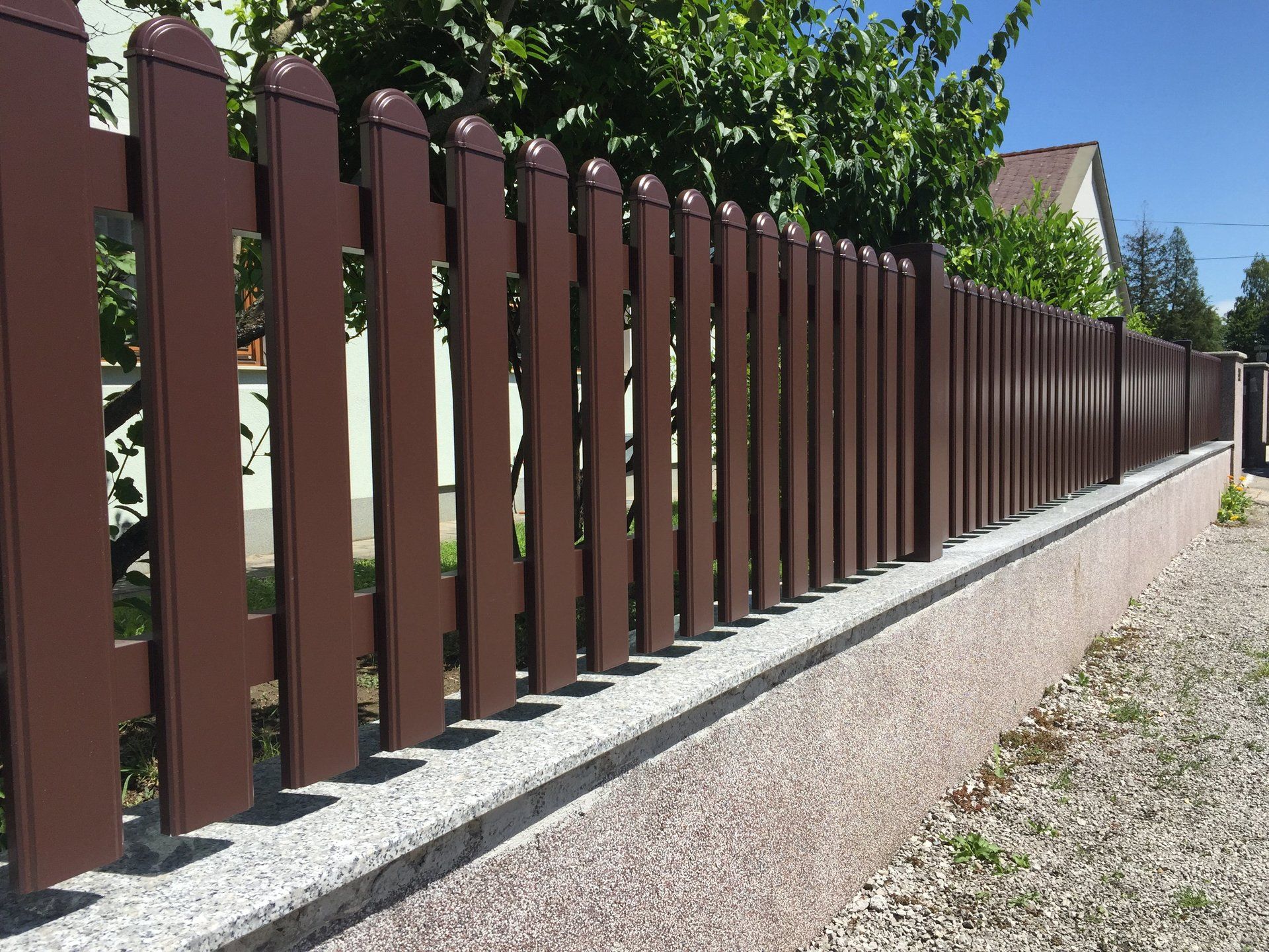 Ein langer brauner Holzzaun entlang einer Schotterstraße.