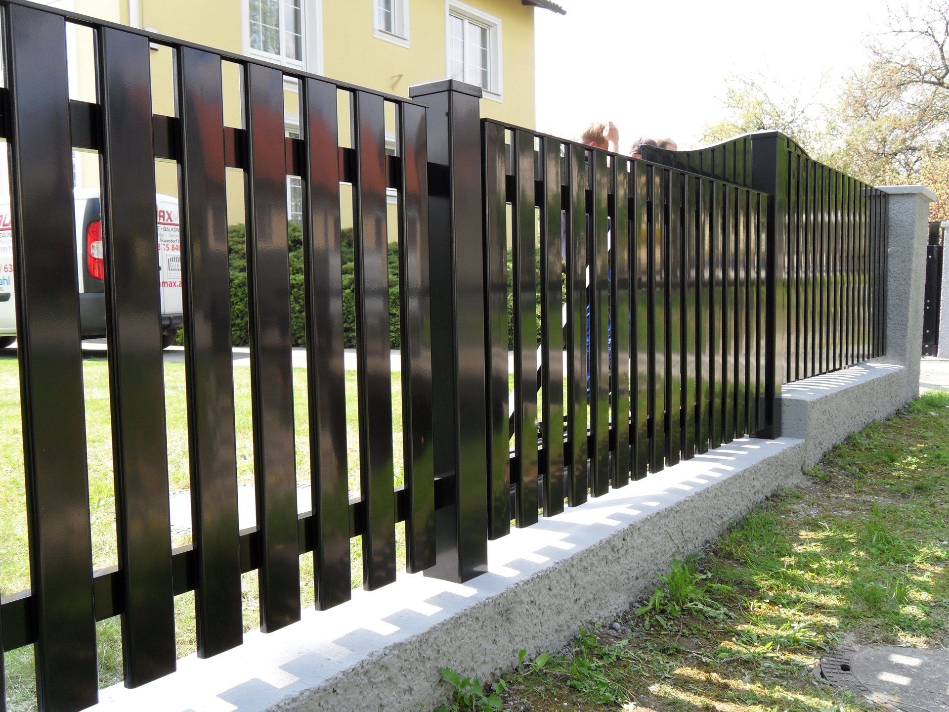 Ein schwarzer Zaun mit einem gelben Haus im Hintergrund