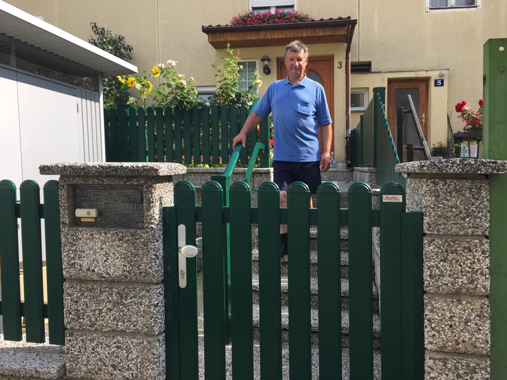 Ein Mann in einem blauen Hemd steht vor einem grünen Zaun