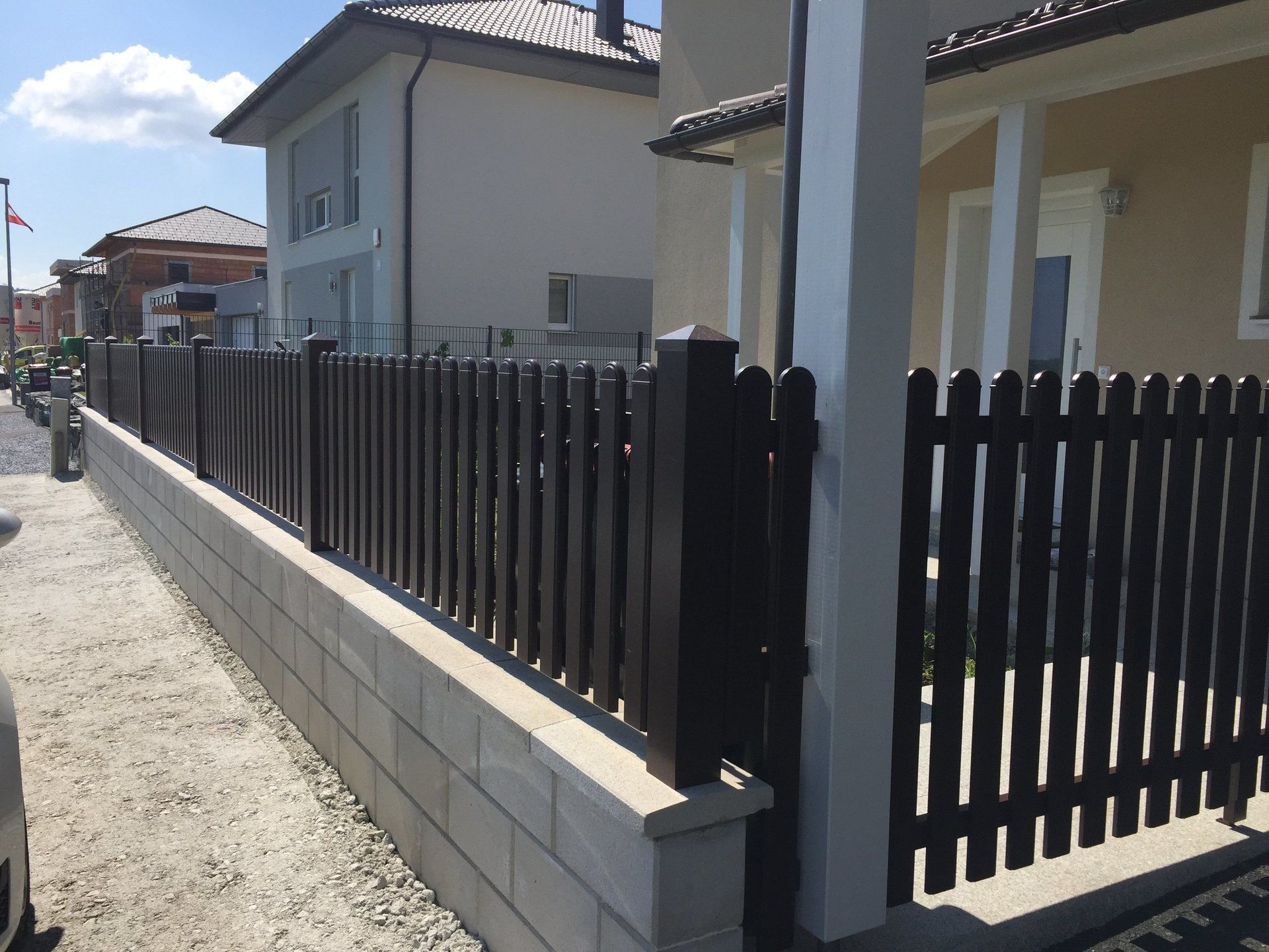 Ein schwarzer Lattenzaun umgibt eine Backsteinmauer vor einem Haus