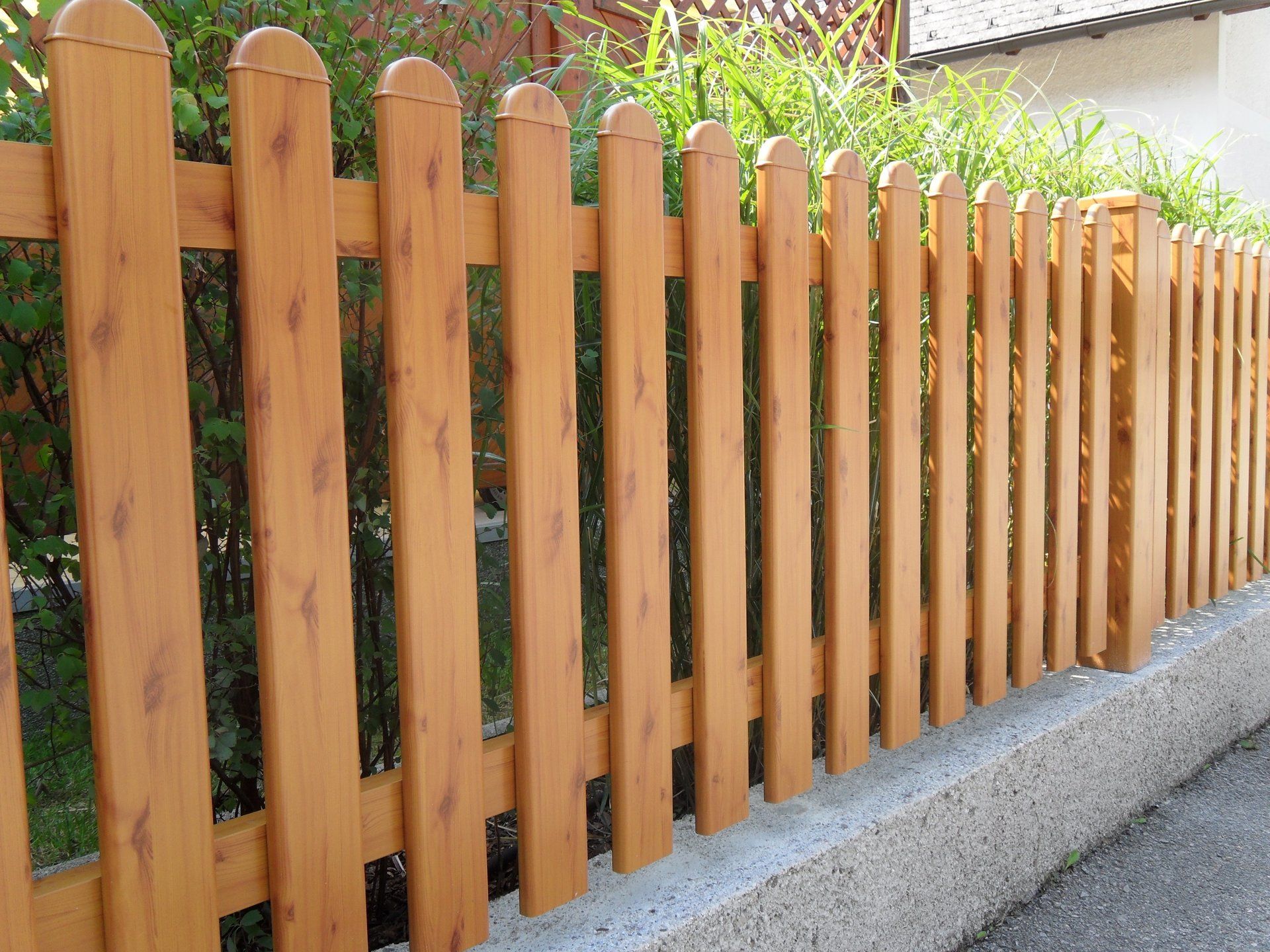 Ein Holzzaun steht am Straßenrand neben einem Busch.