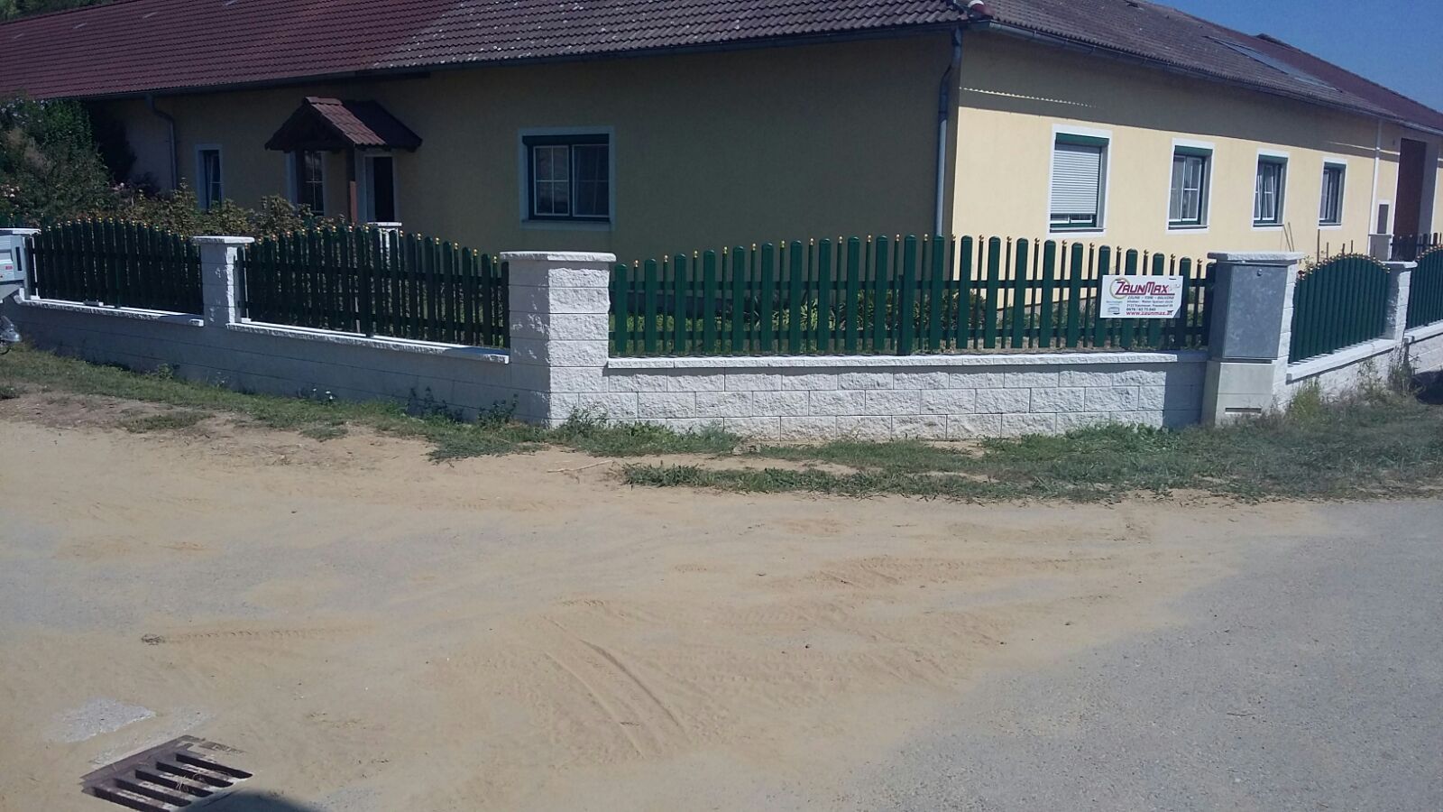 Ein gelbes Haus mit einem grünen Zaun drumherum.