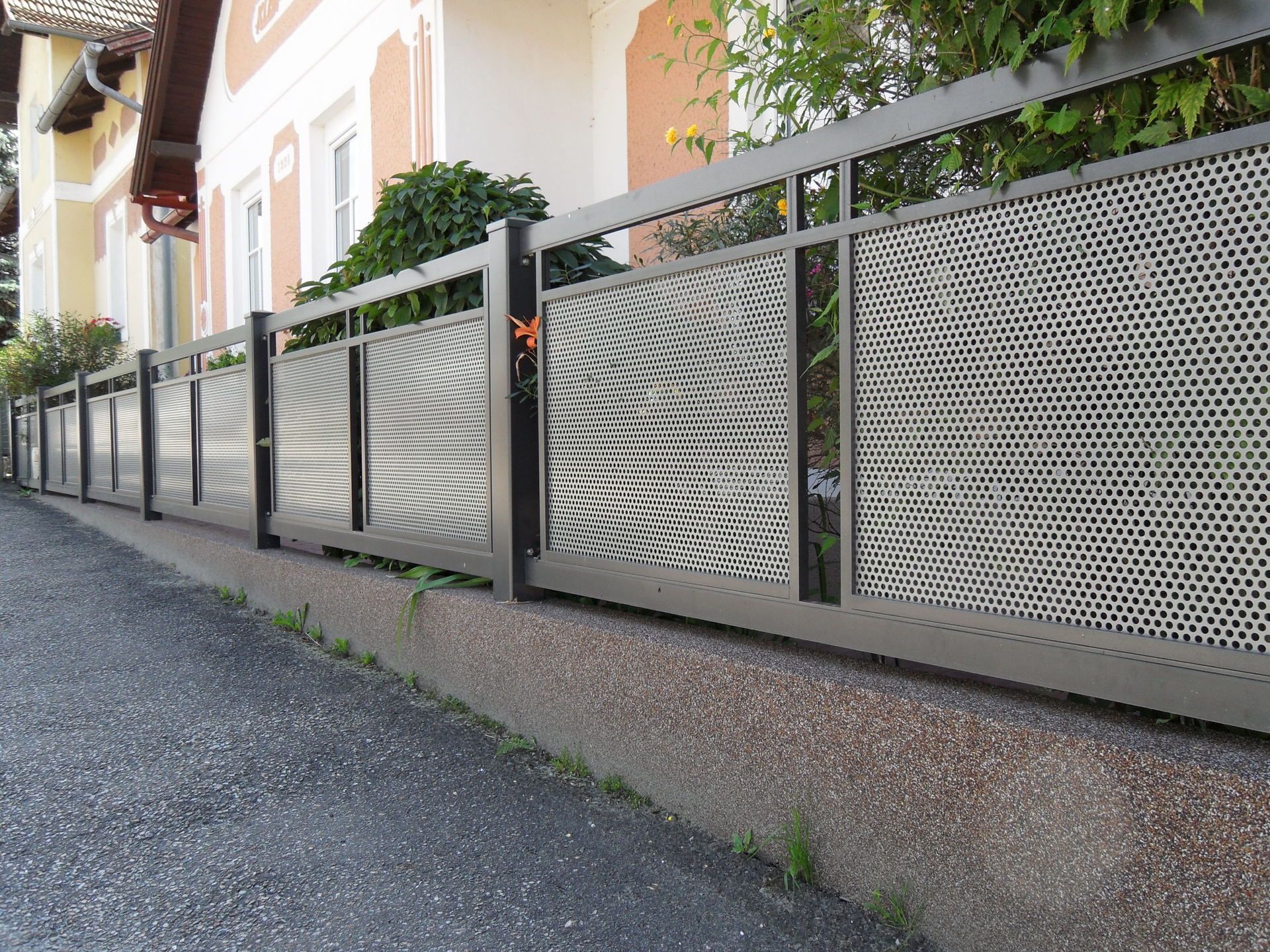 Vor einem Haus steht am Straßenrand ein Metallzaun.