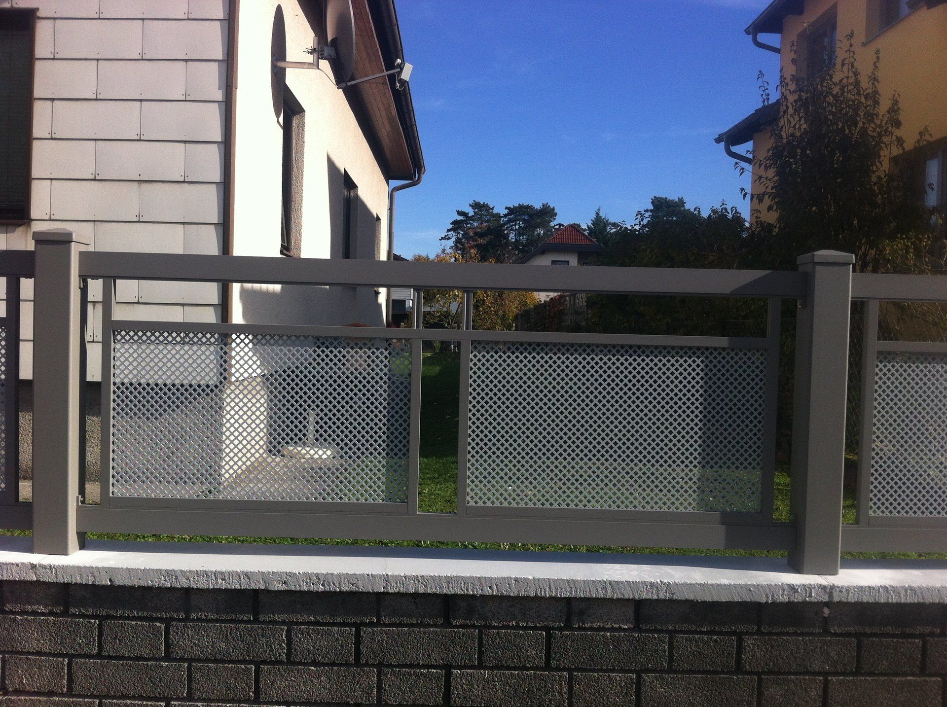 Ein Zaun umgibt eine Backsteinmauer vor einem Haus