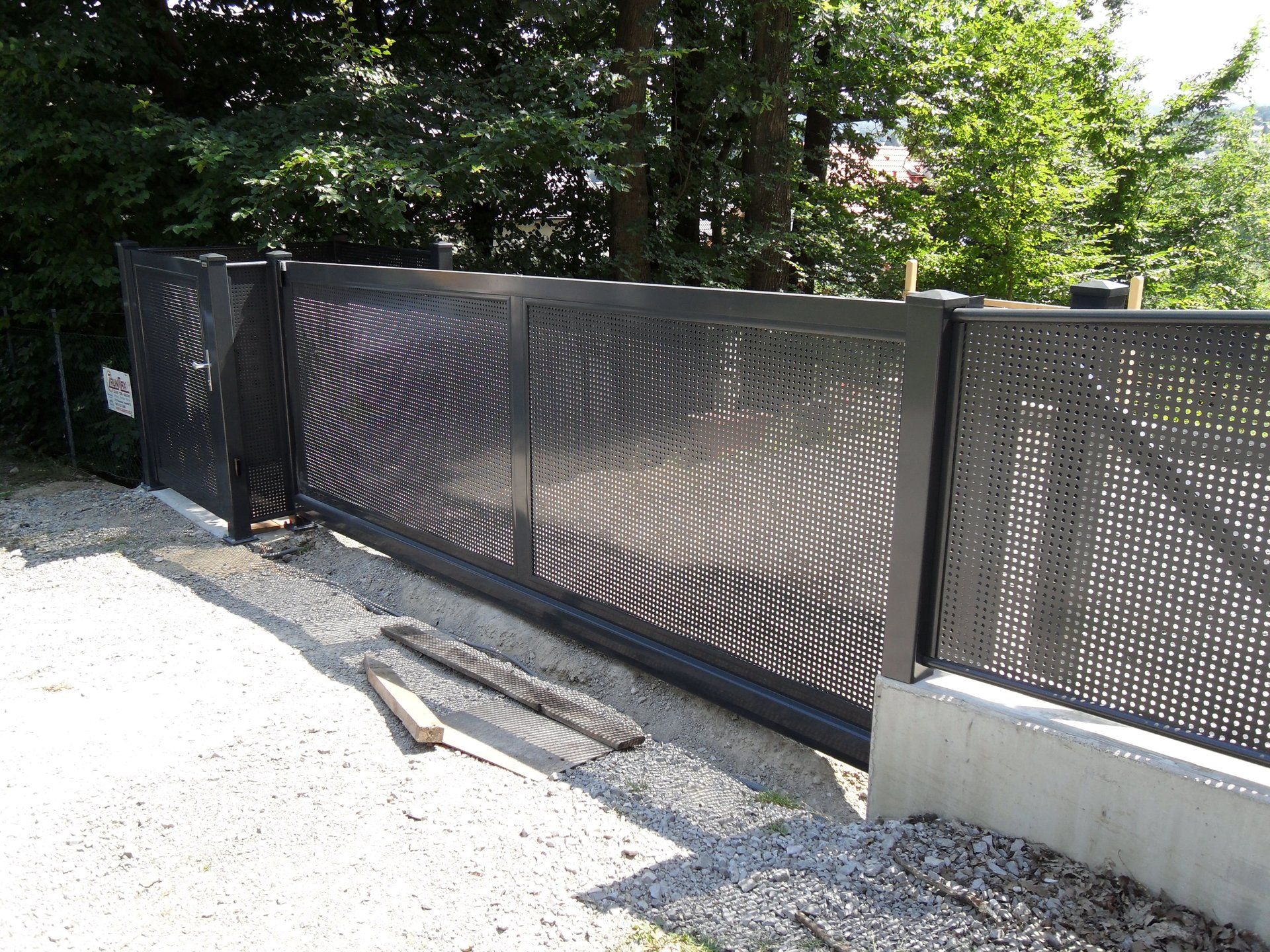 Auf einer Schotterstraße steht ein schwarzer Metallzaun.