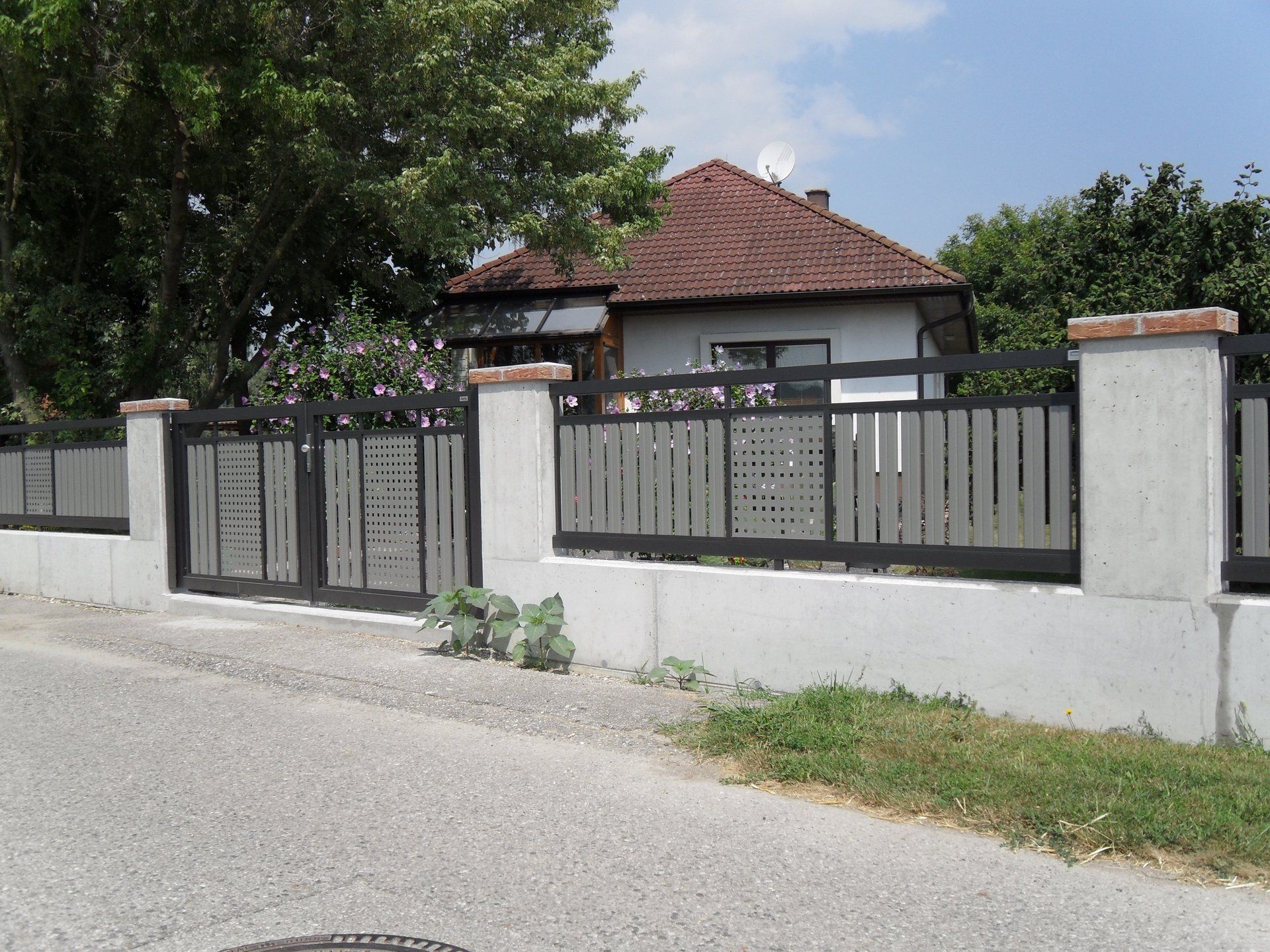 Hinter einem Zaun steht ein Haus mit rotem Ziegeldach