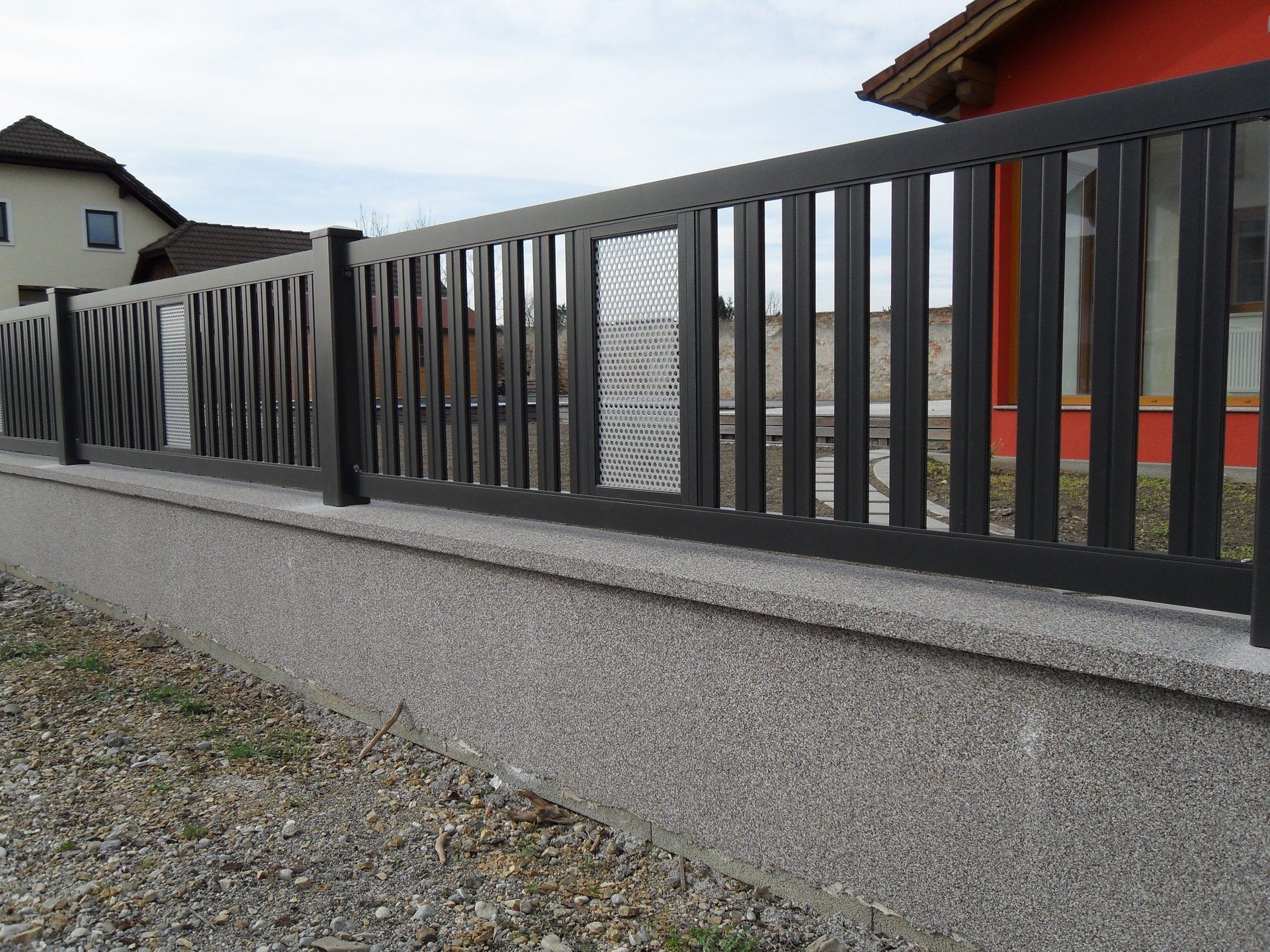 Ein schwarzer Zaun mit einem roten Haus im Hintergrund