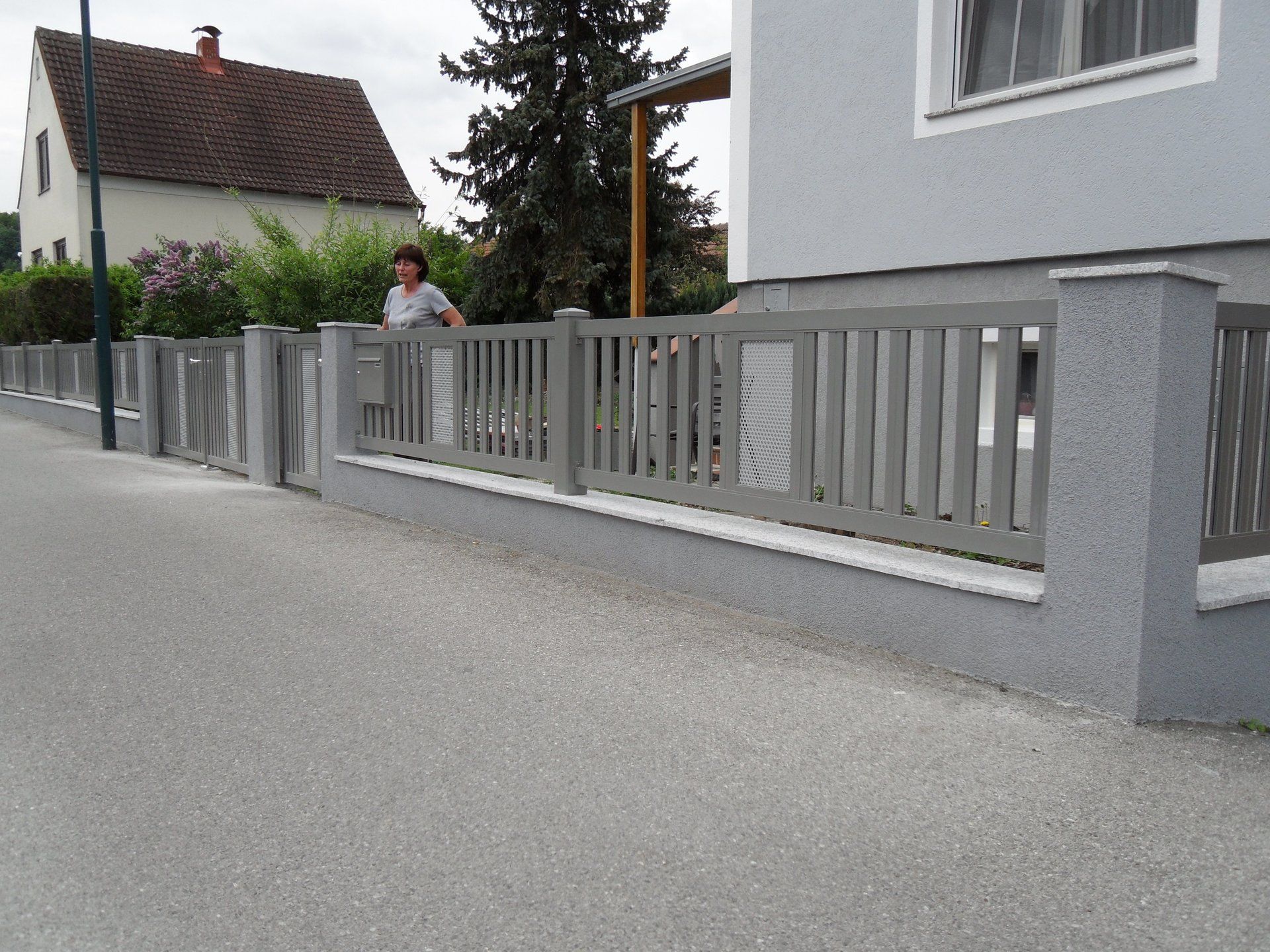 Eine Frau steht vor einem Zaun neben einem Haus