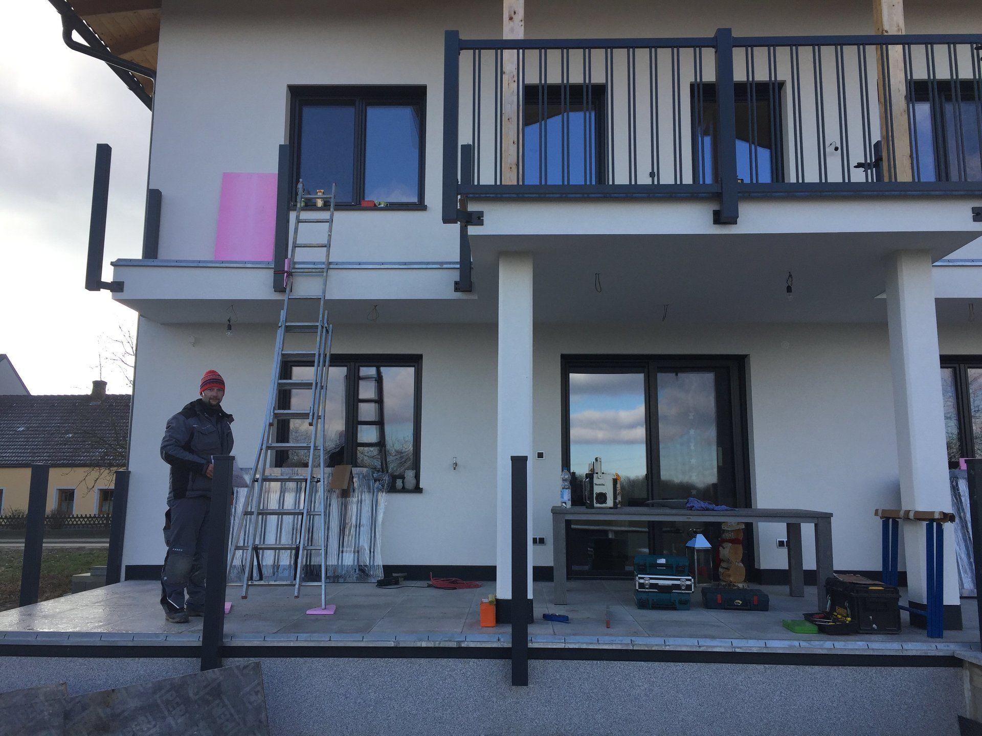 Ein Mann steht mit einer Leiter auf einer Veranda vor einem Haus.
