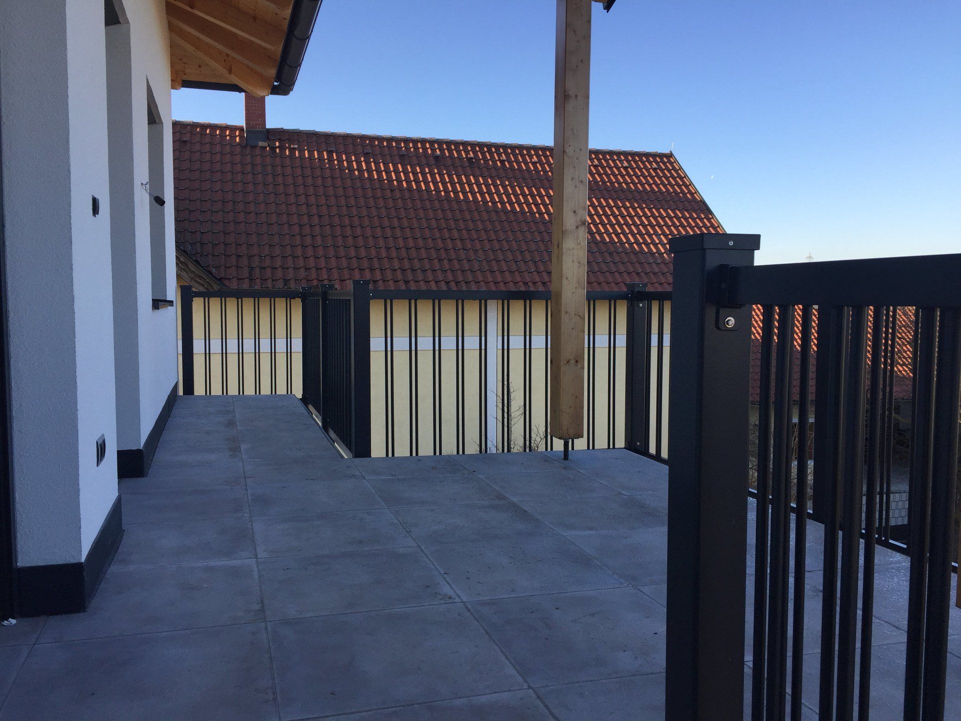 Ein Balkon mit schwarzem Geländer und Dach im Hintergrund.