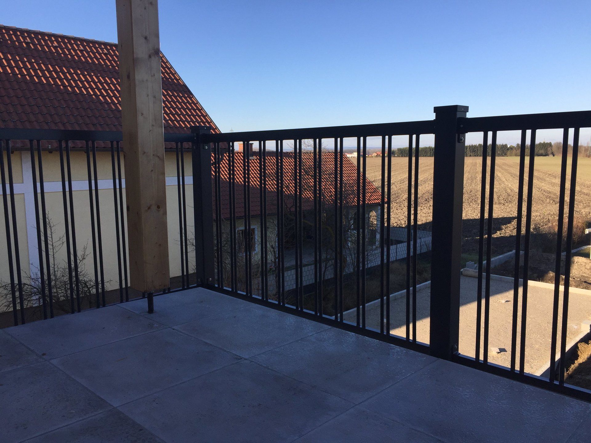 Ein Balkon mit schwarzem Geländer und Blick auf ein Feld.