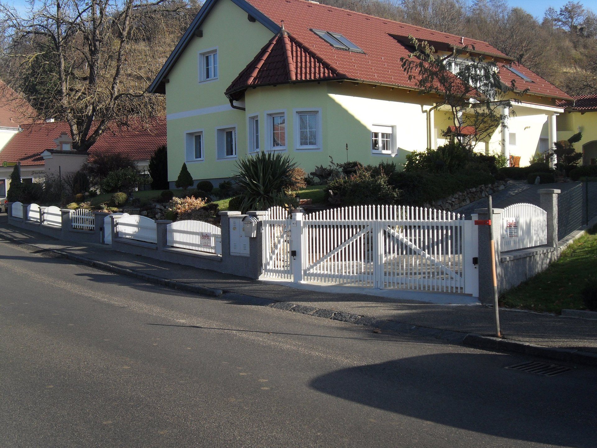 Ein gelbes Haus mit einem roten Dach und einem weißen Zaun