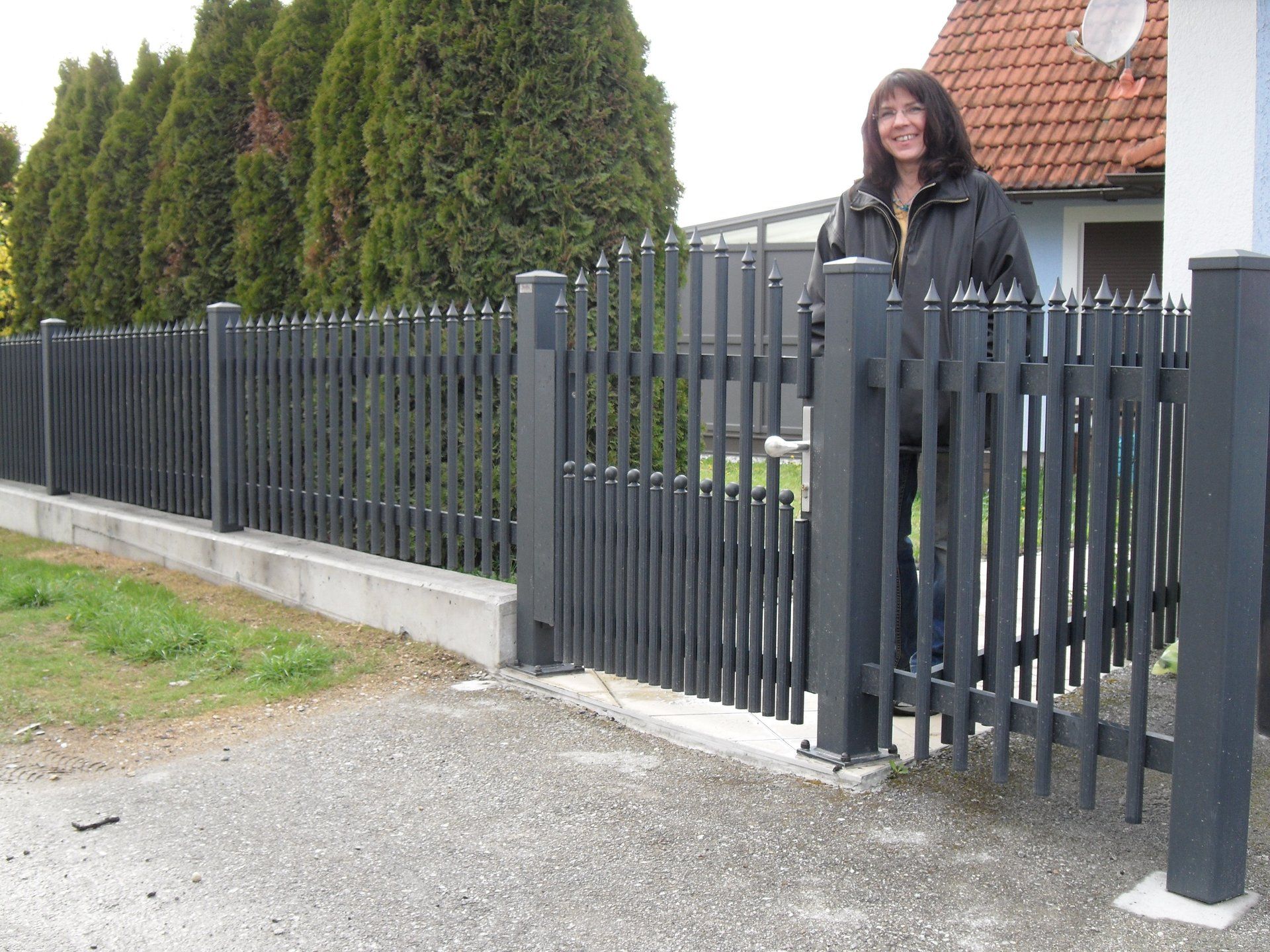 Eine Frau steht hinter einem schwarzen Zaun vor einem Haus