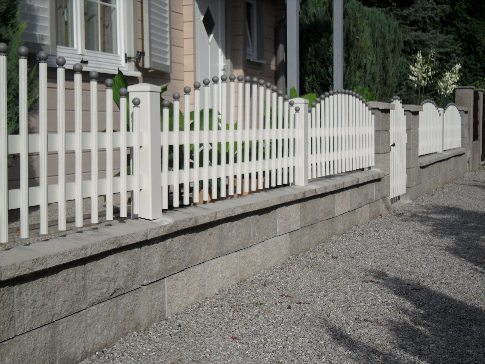 Ein weißer Lattenzaun umgibt eine Kiesauffahrt vor einem Haus