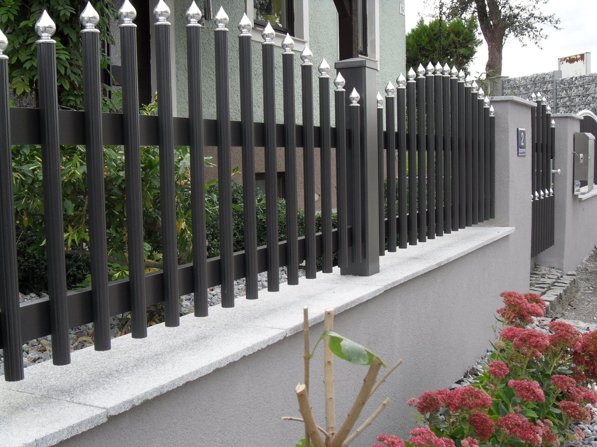 Ein schwarzer Zaun umgibt ein Haus mit Blumen davor