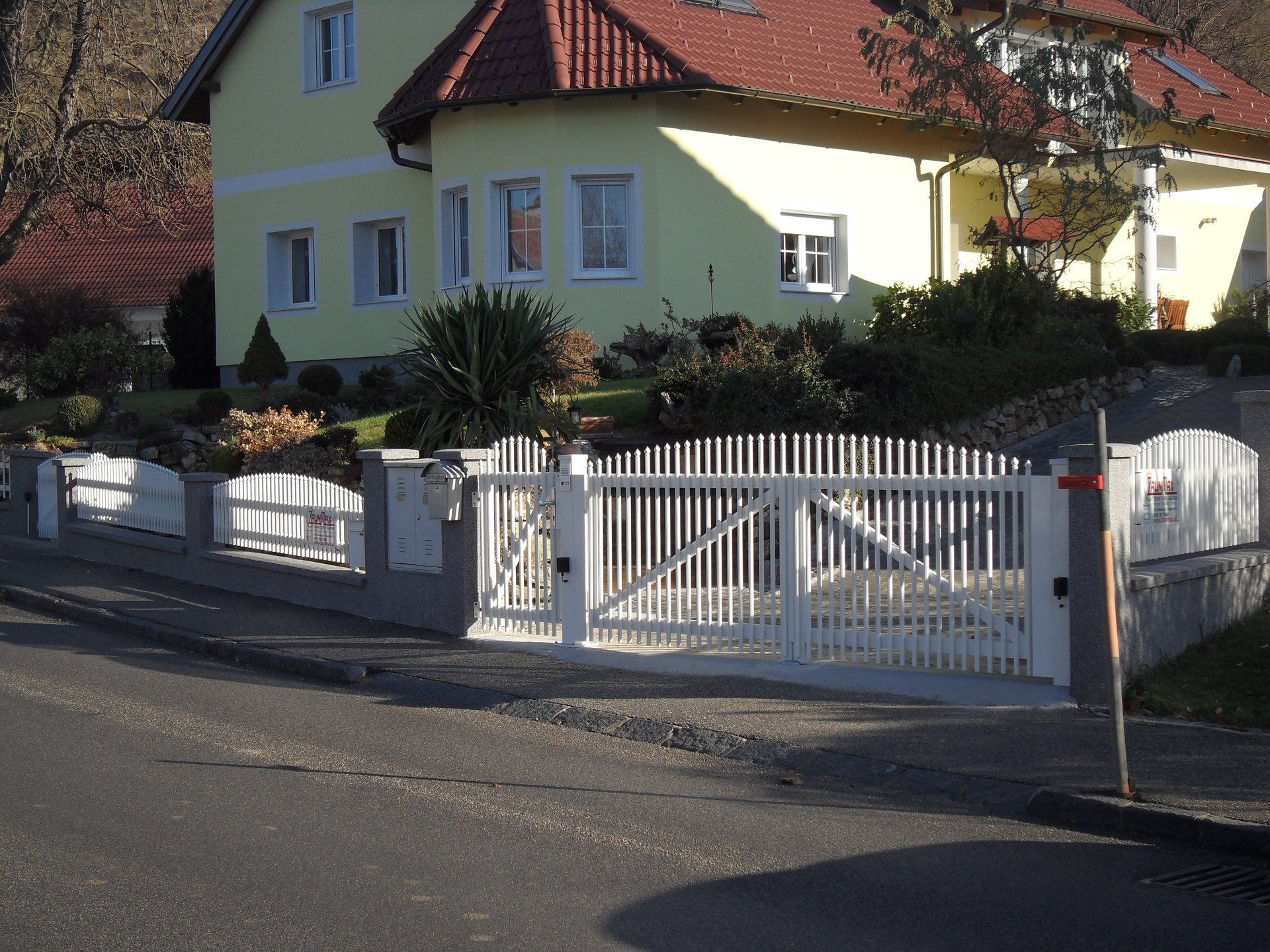 Ein gelbes Haus mit einem roten Dach und einem weißen Zaun