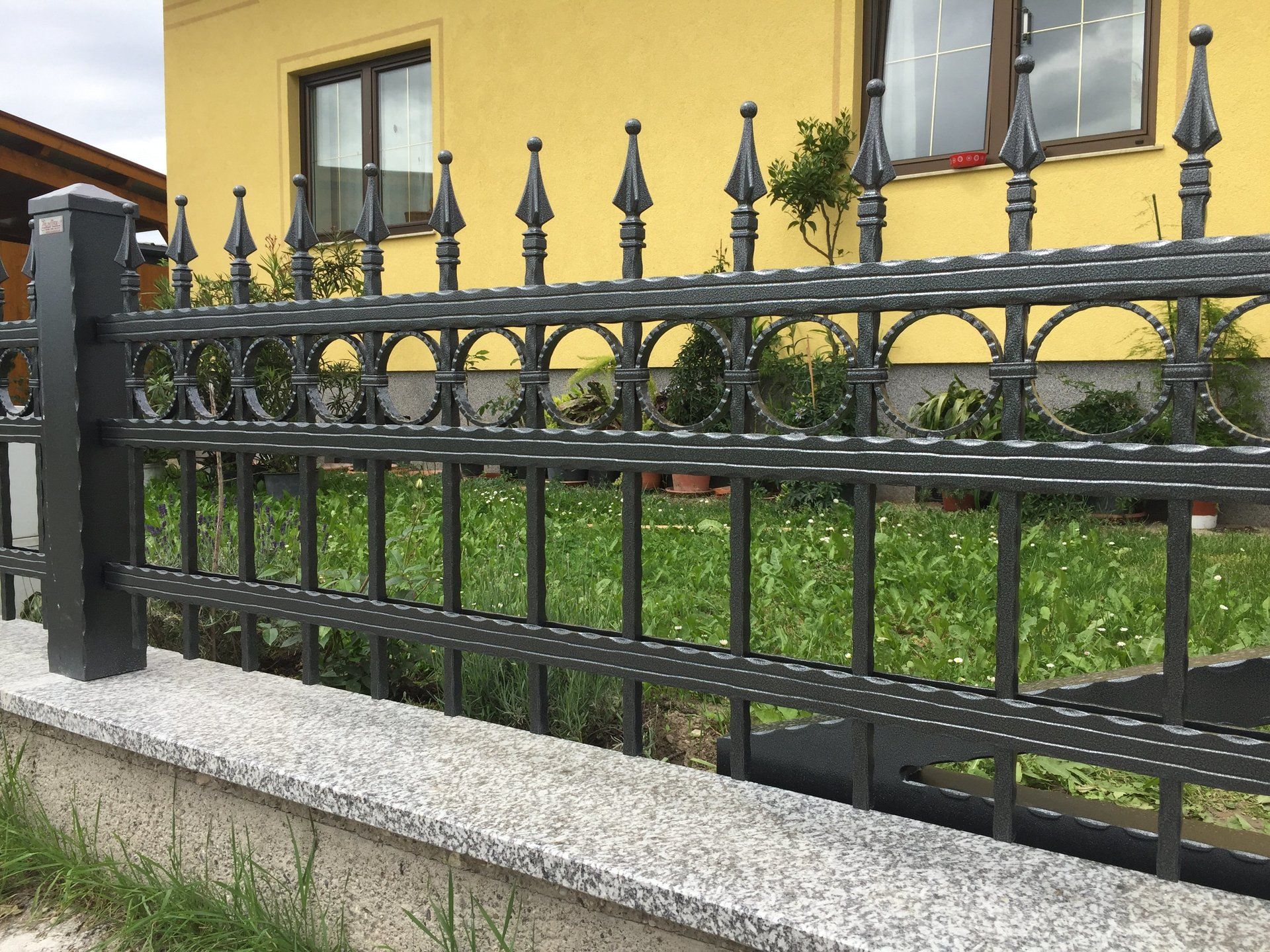 Vor einem gelben Haus steht ein schmiedeeiserner Zaun.