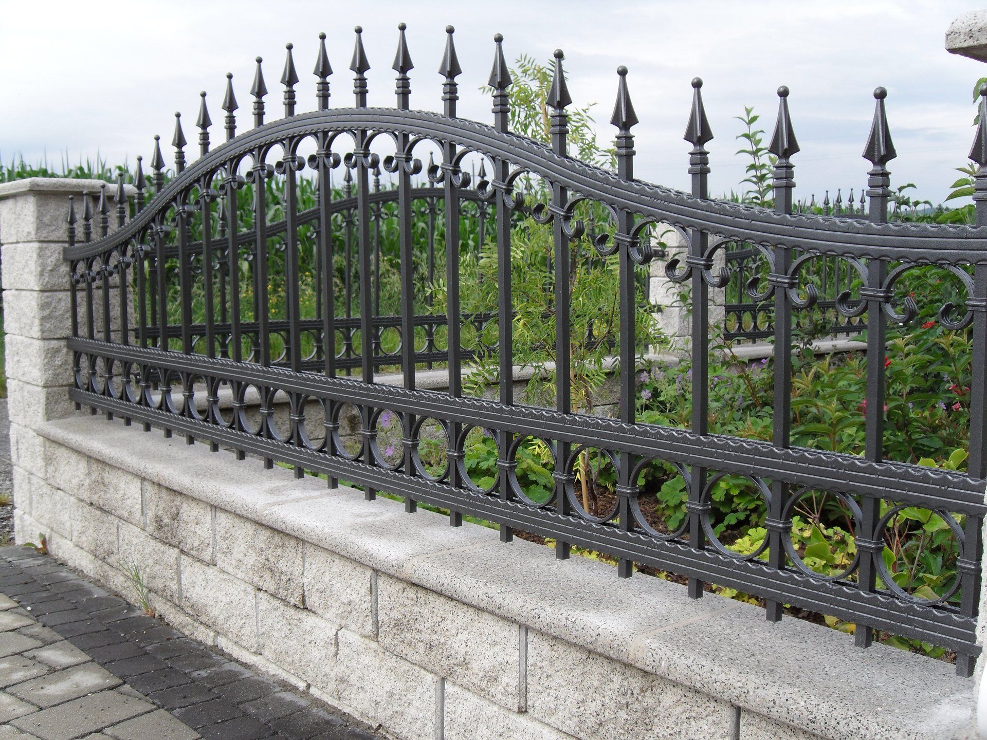 Ein schmiedeeiserner Zaun umgibt eine Backsteinmauer.