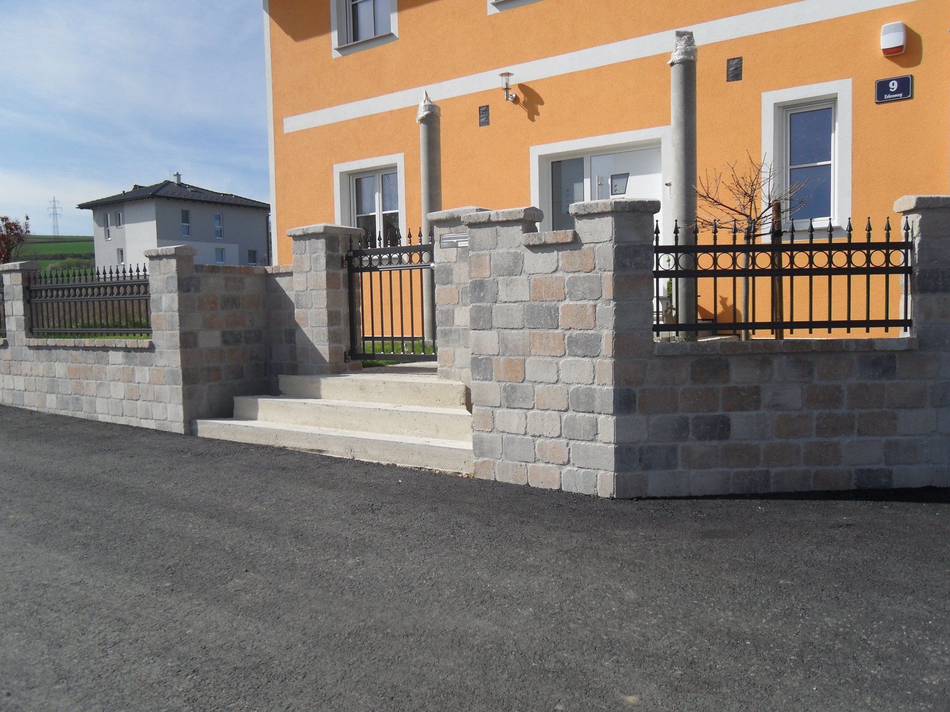 Ein Haus mit einer Backsteinmauer und einem schwarzen Zaun