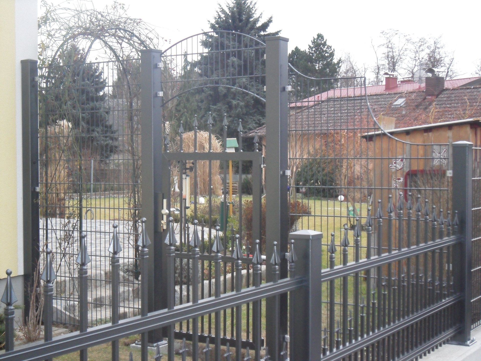 Ein schmiedeeiserner Zaun umgibt einen Garten mit einem Haus im Hintergrund