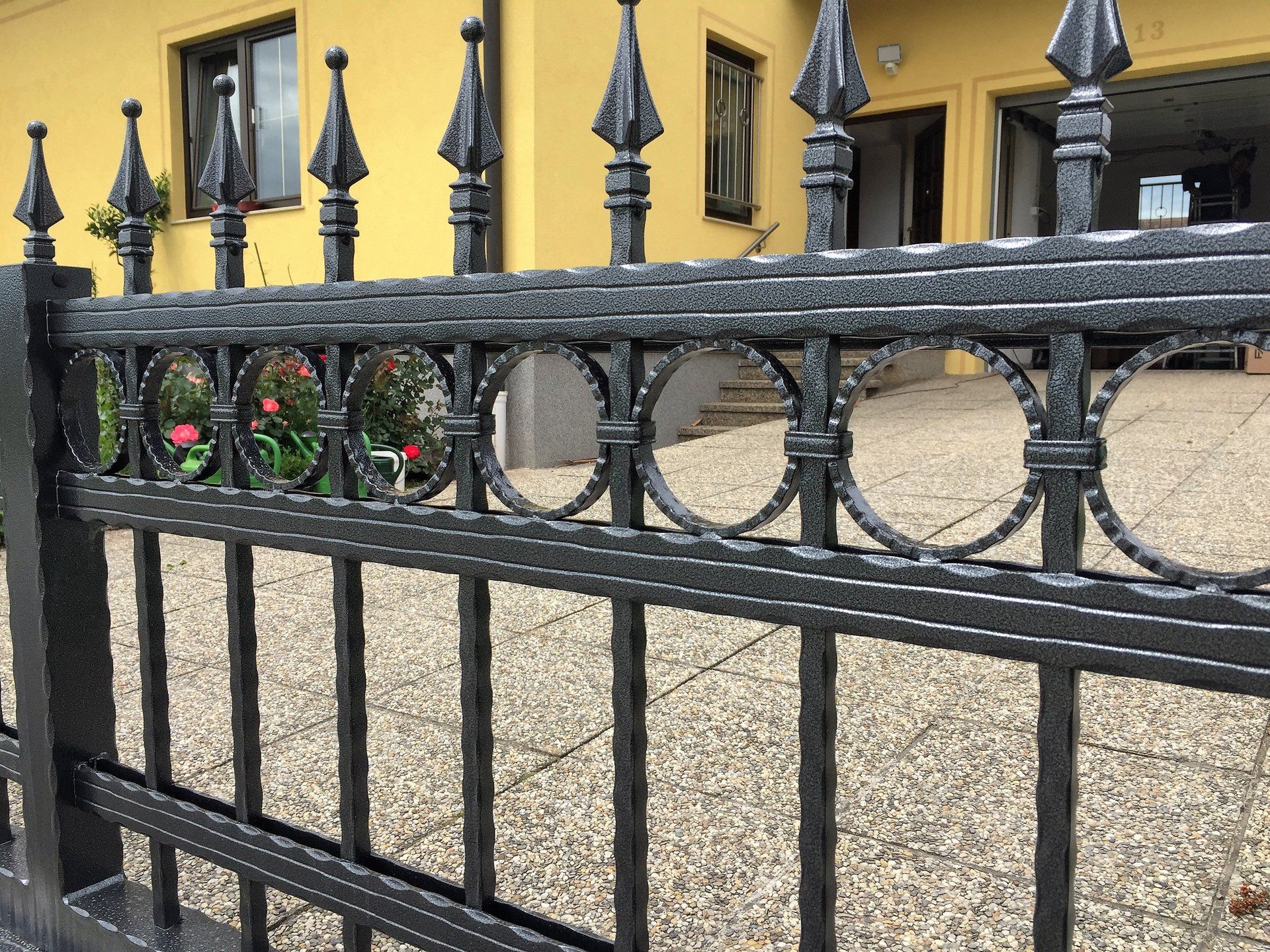 Ein schmiedeeiserner Zaun steht vor einem gelben Haus