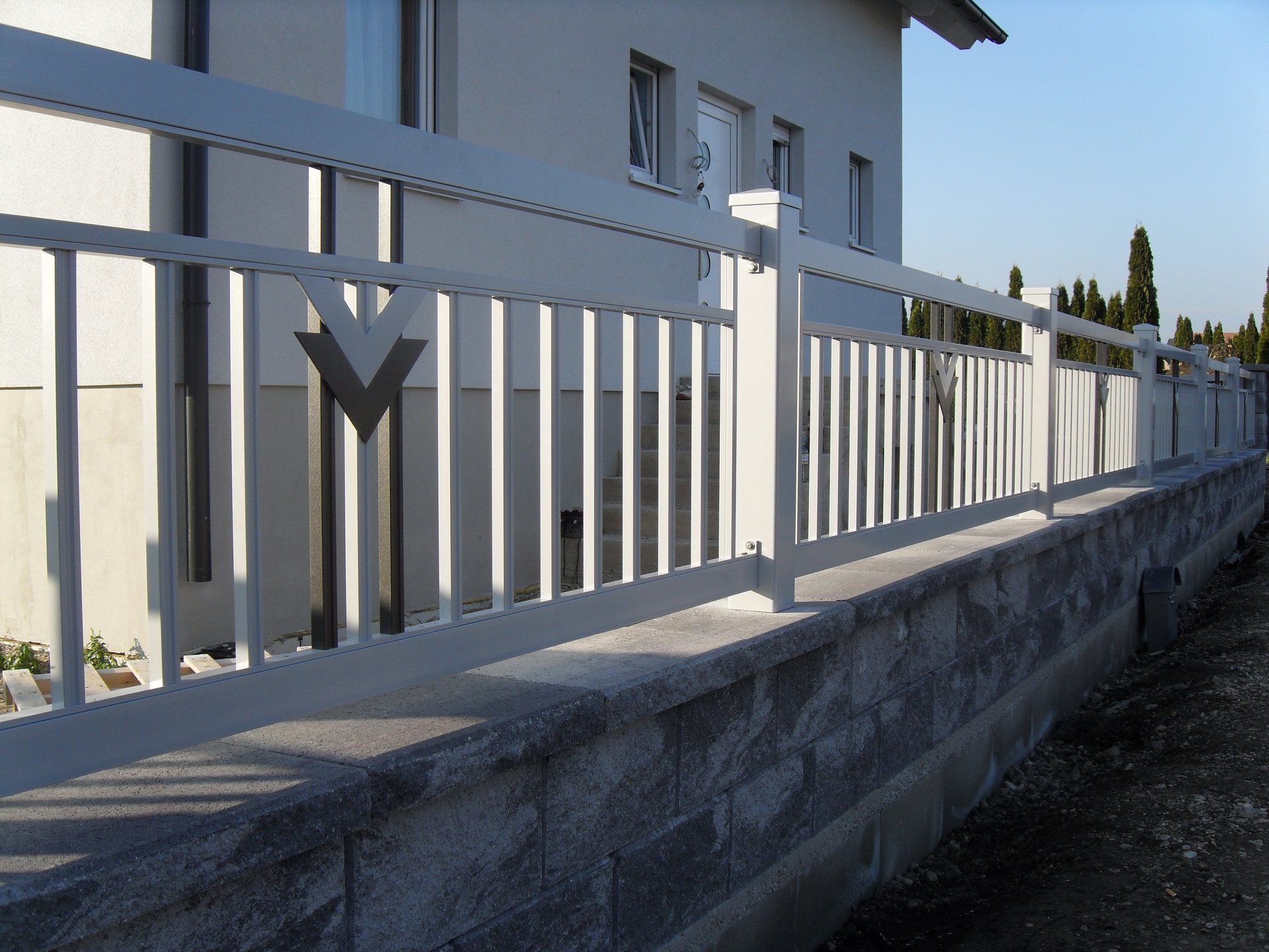 Ein weißer Zaun umgibt eine Steinmauer vor einem Haus