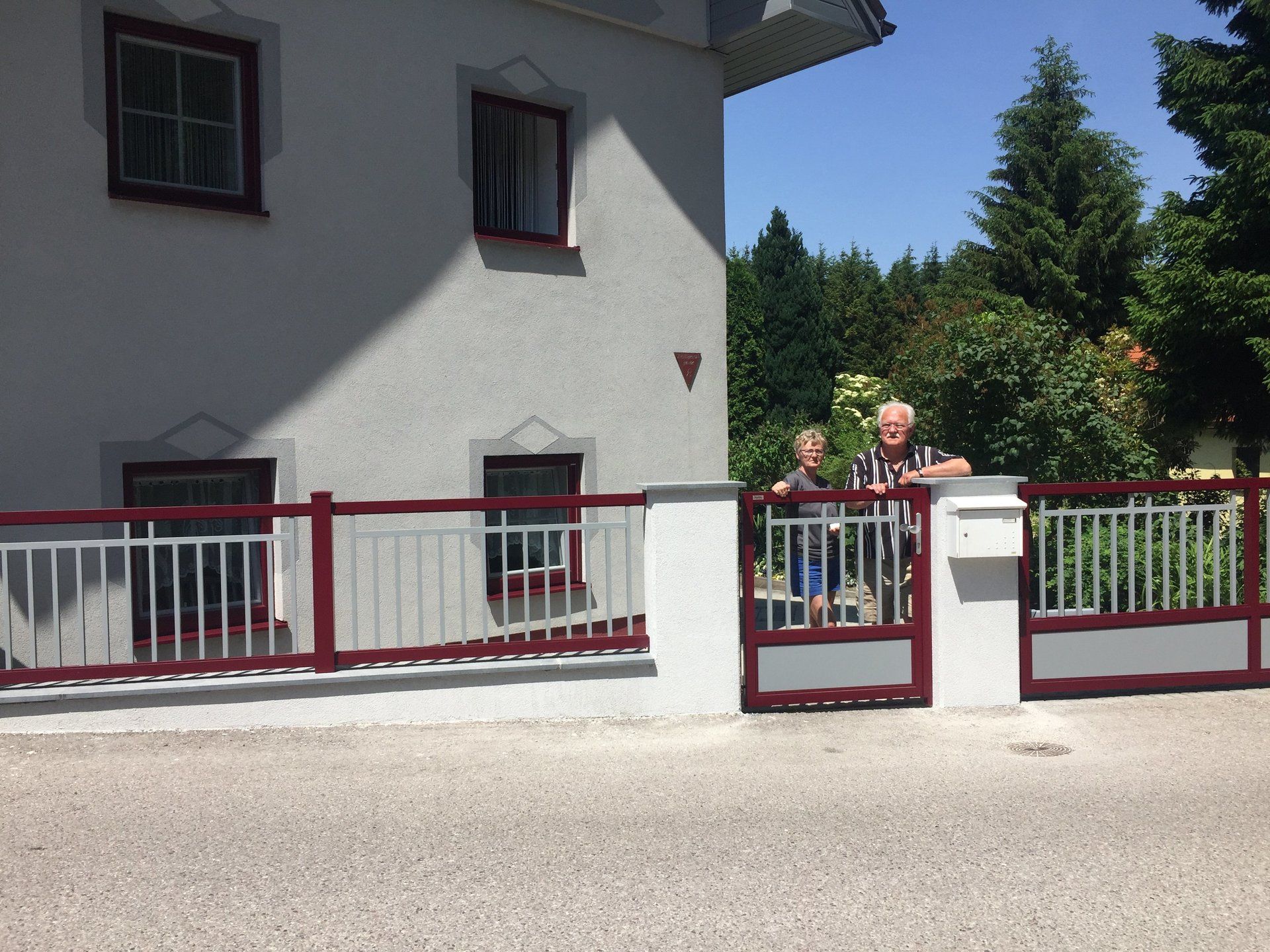 Ein Paar steht vor einem weißen Haus mit einem roten Zaun