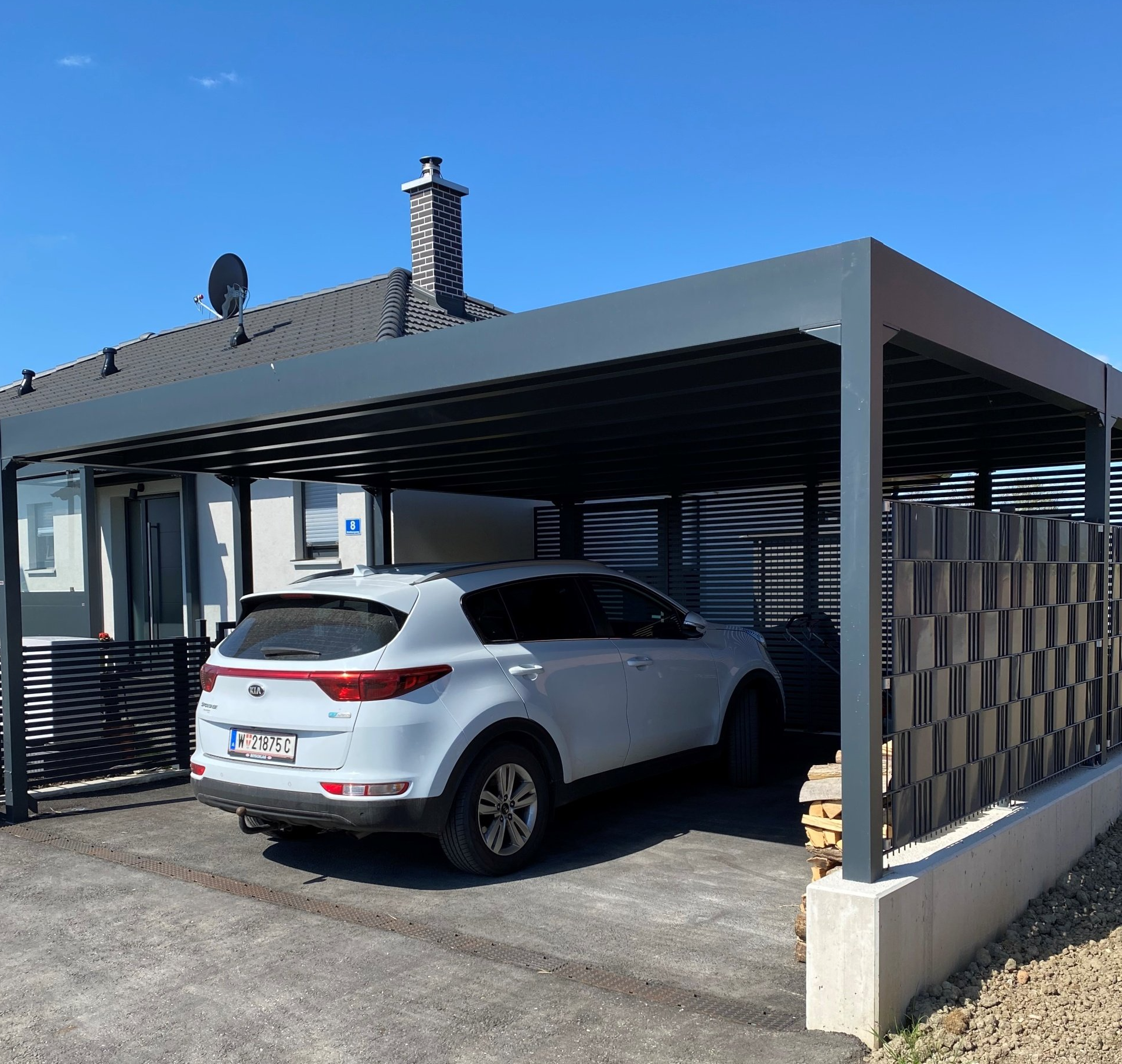 Ein weißes Auto steht unter einem Carport vor einem Haus