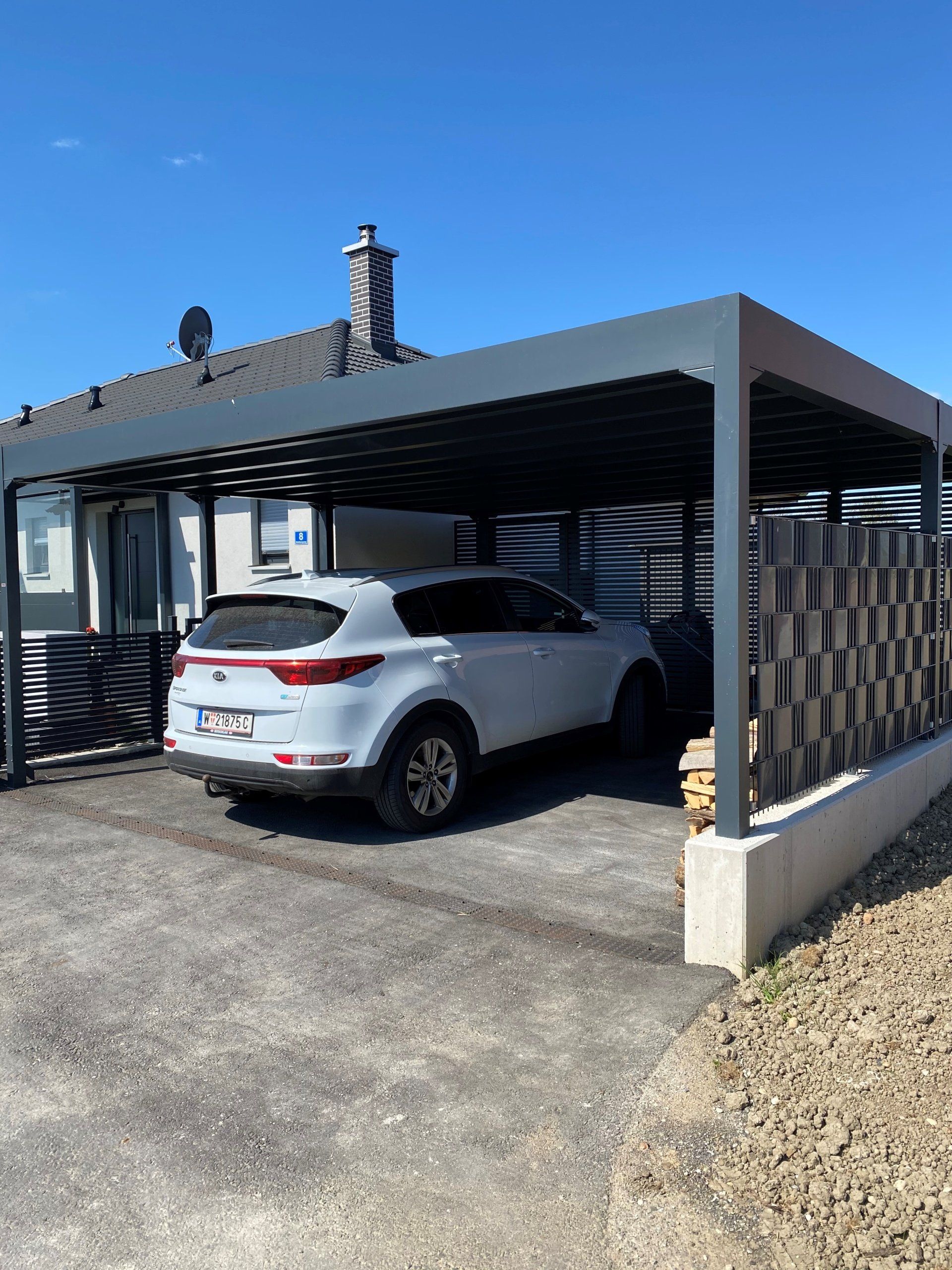 Ein weißes Auto ist unter einem Carport vor einem Haus geparkt.