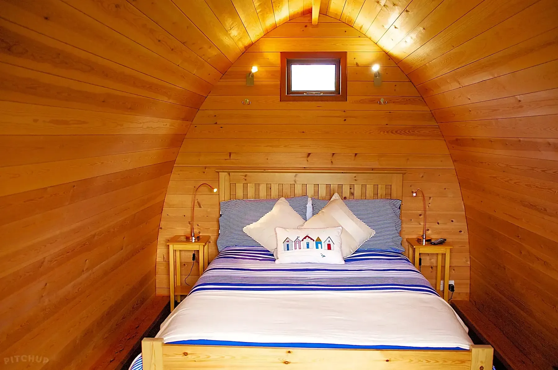 Bedroom with wooden walls, bed with blue and white bedding, two bedside tables.