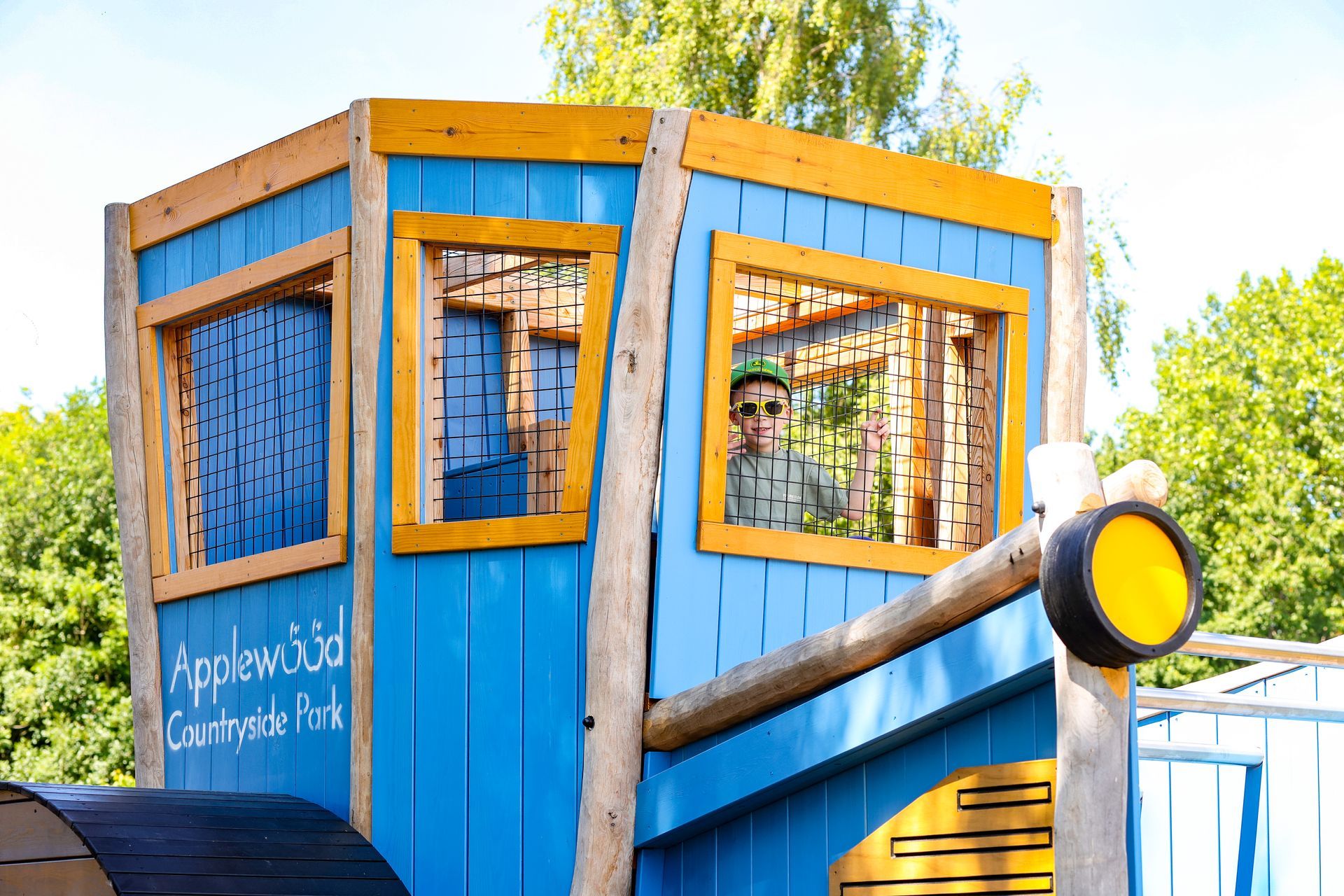 Blue wooden playhouse with yellow trim, a child looking out the window.
