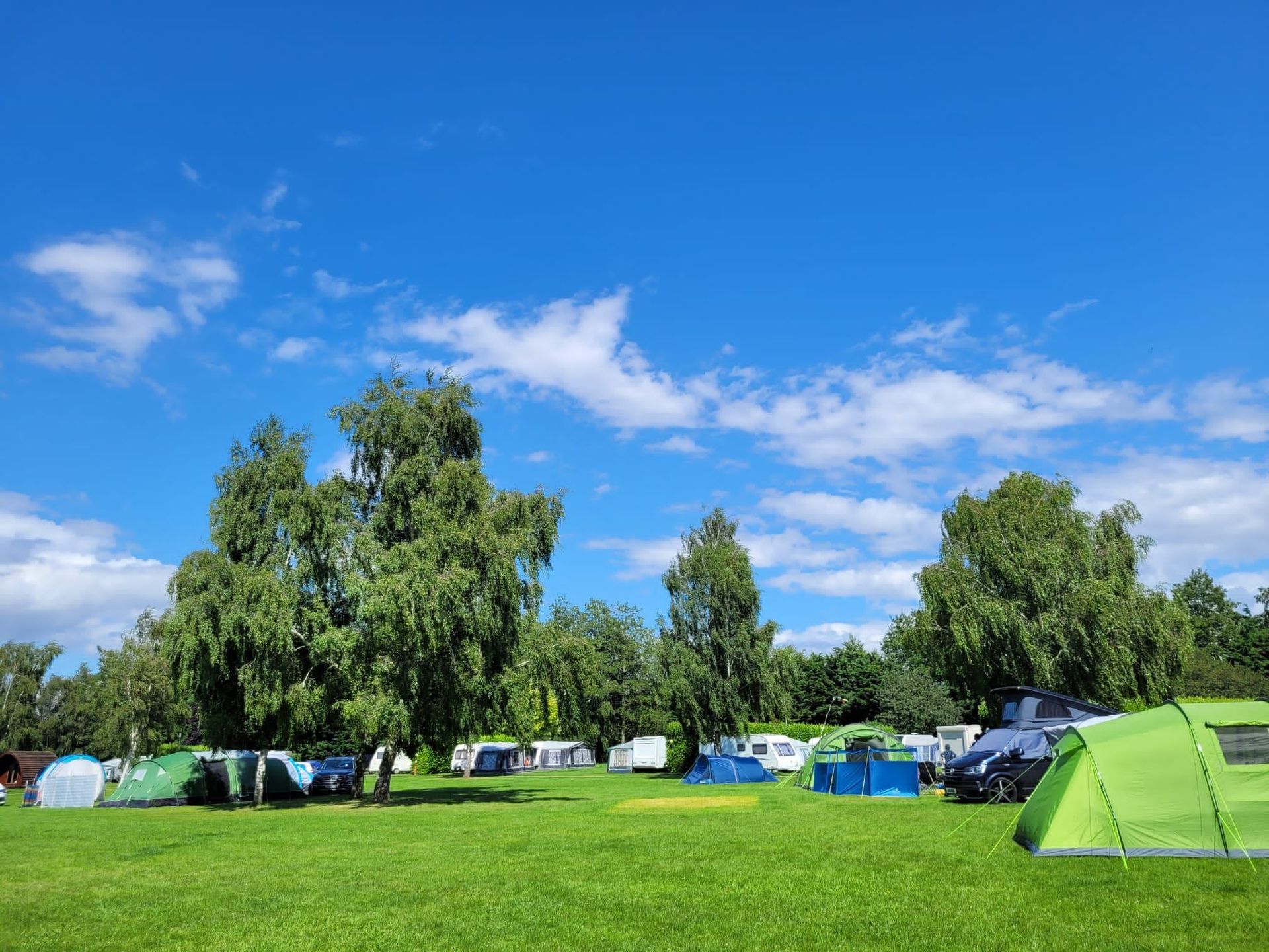 Camping area with tents, trees, and blue sky with clouds.