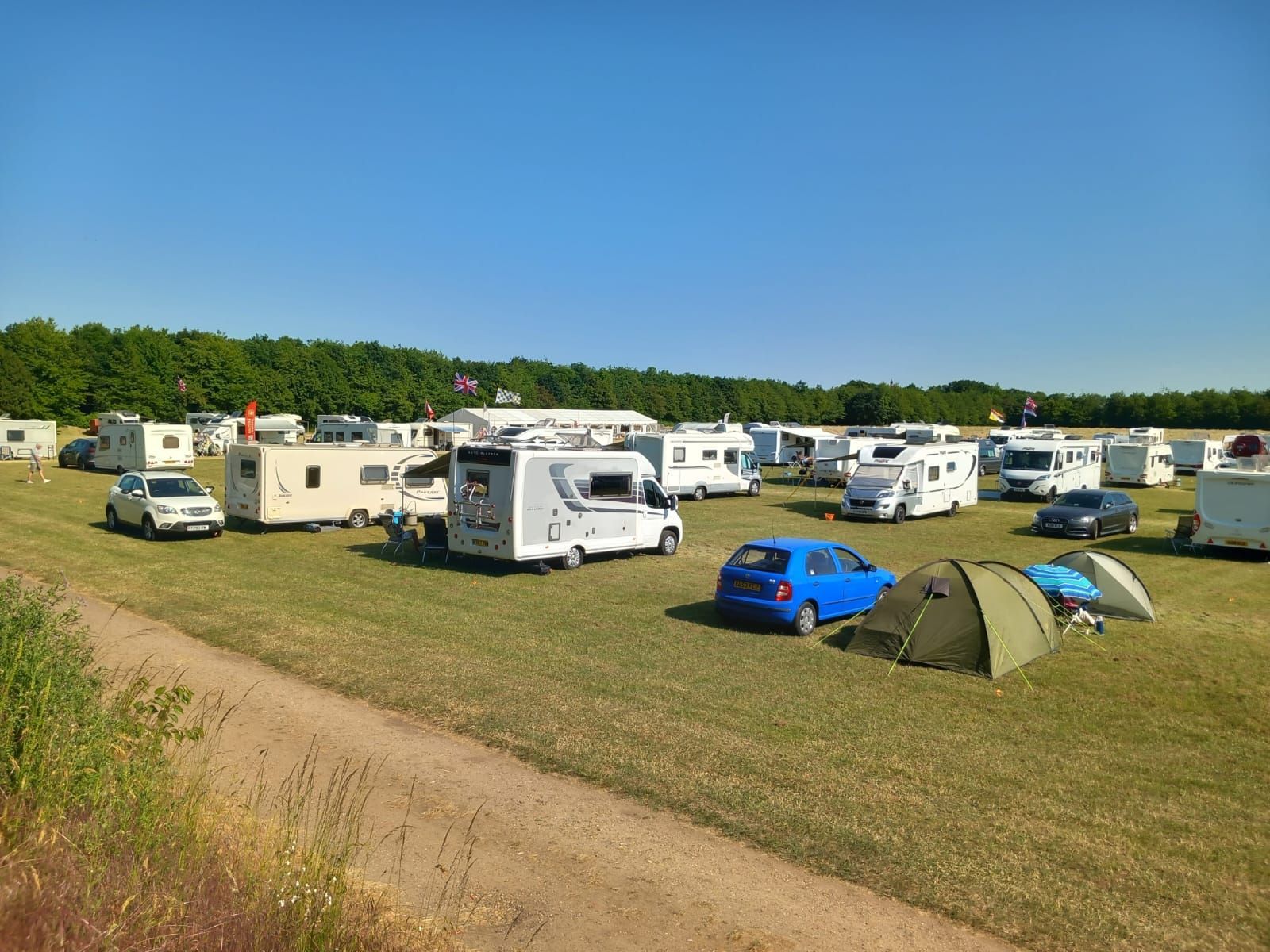 Campground with many RVs, cars, and tents on a grassy field under a clear blue sky.