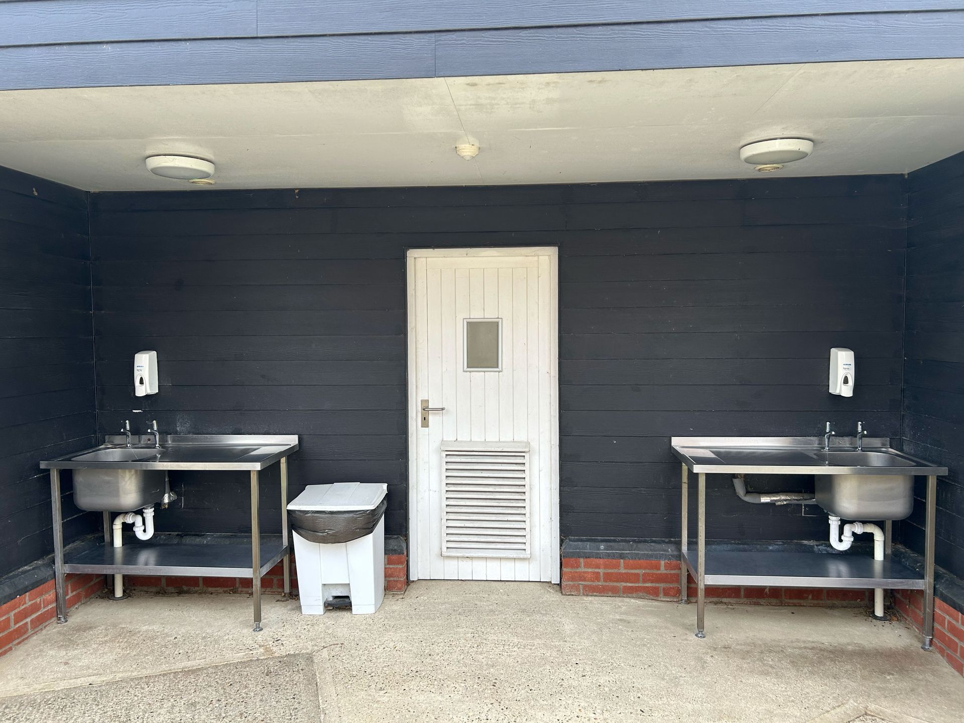 Outdoor cleaning station with two sinks, hand soap dispensers, and a door.