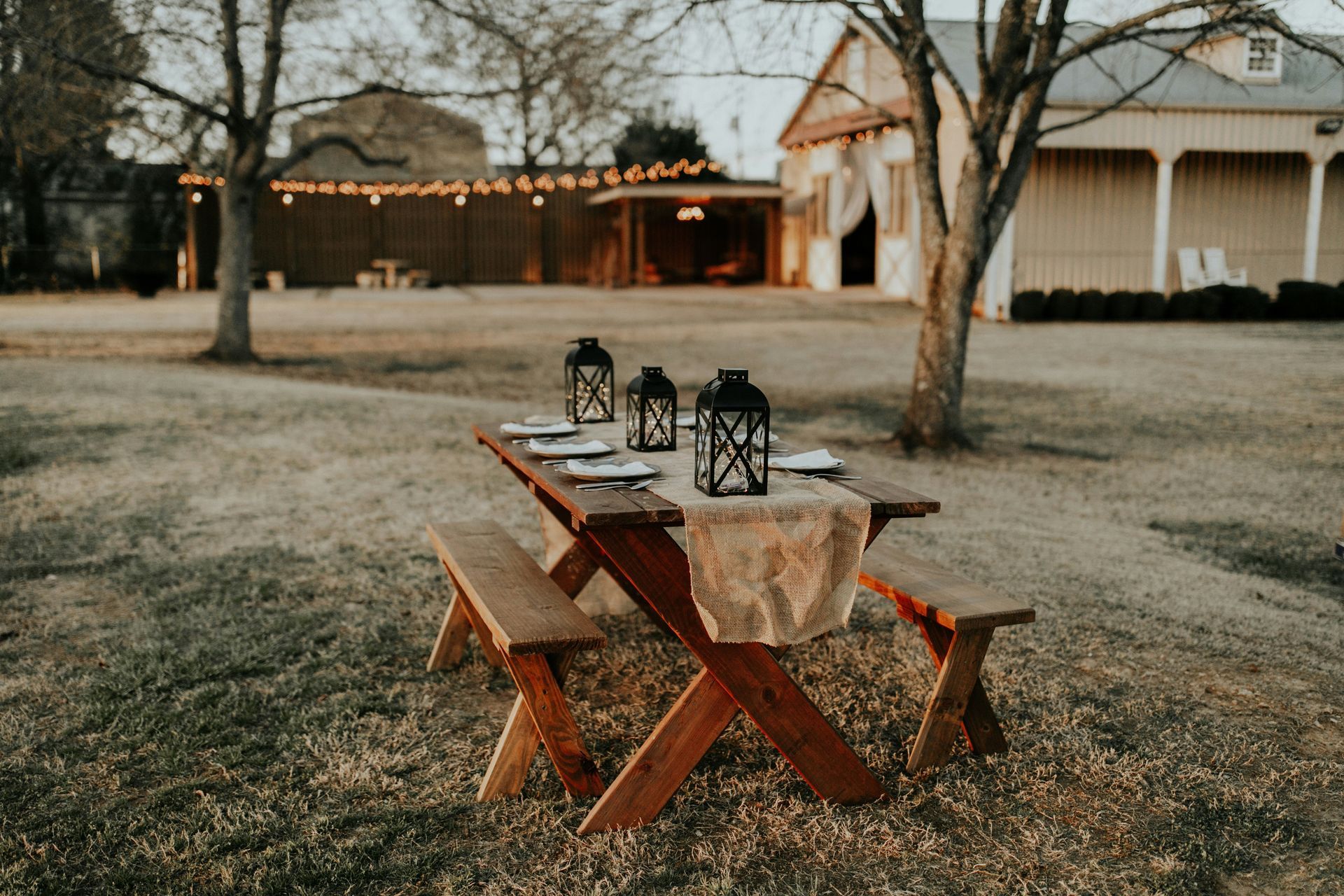 A wooden picnic table with lanterns on it in a field.