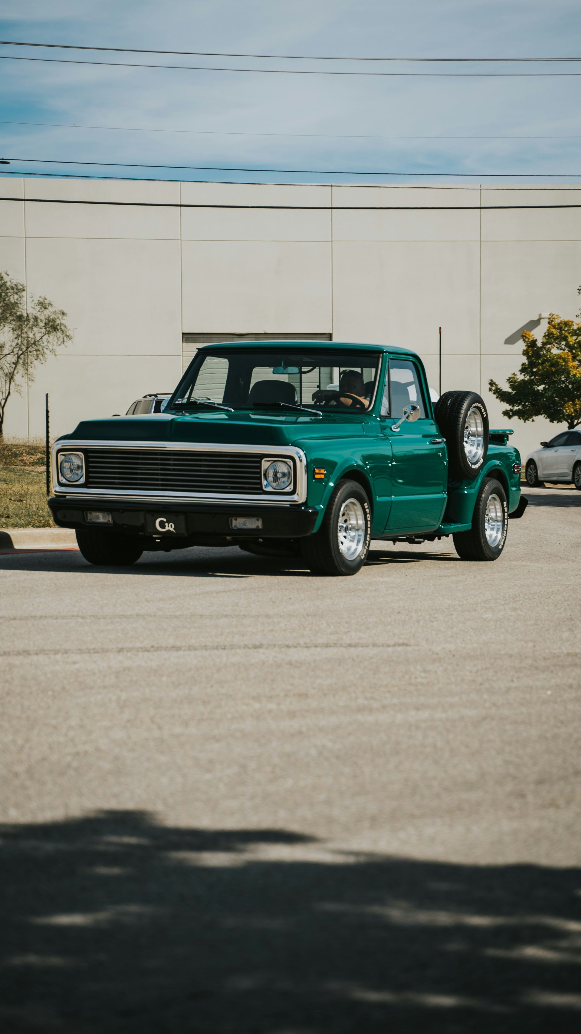 A green truck is parked in a parking lot in front of a building.