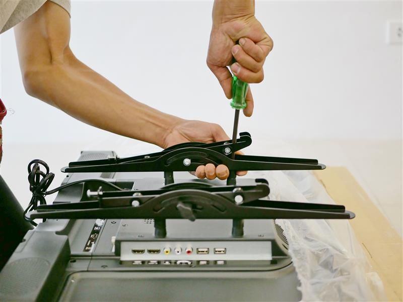 Person using a screwdriver to attach brackets to the back of a TV.