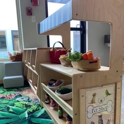 Wooden pretend pet shop with baskets of toy fruits and vegetables in a bright playroom